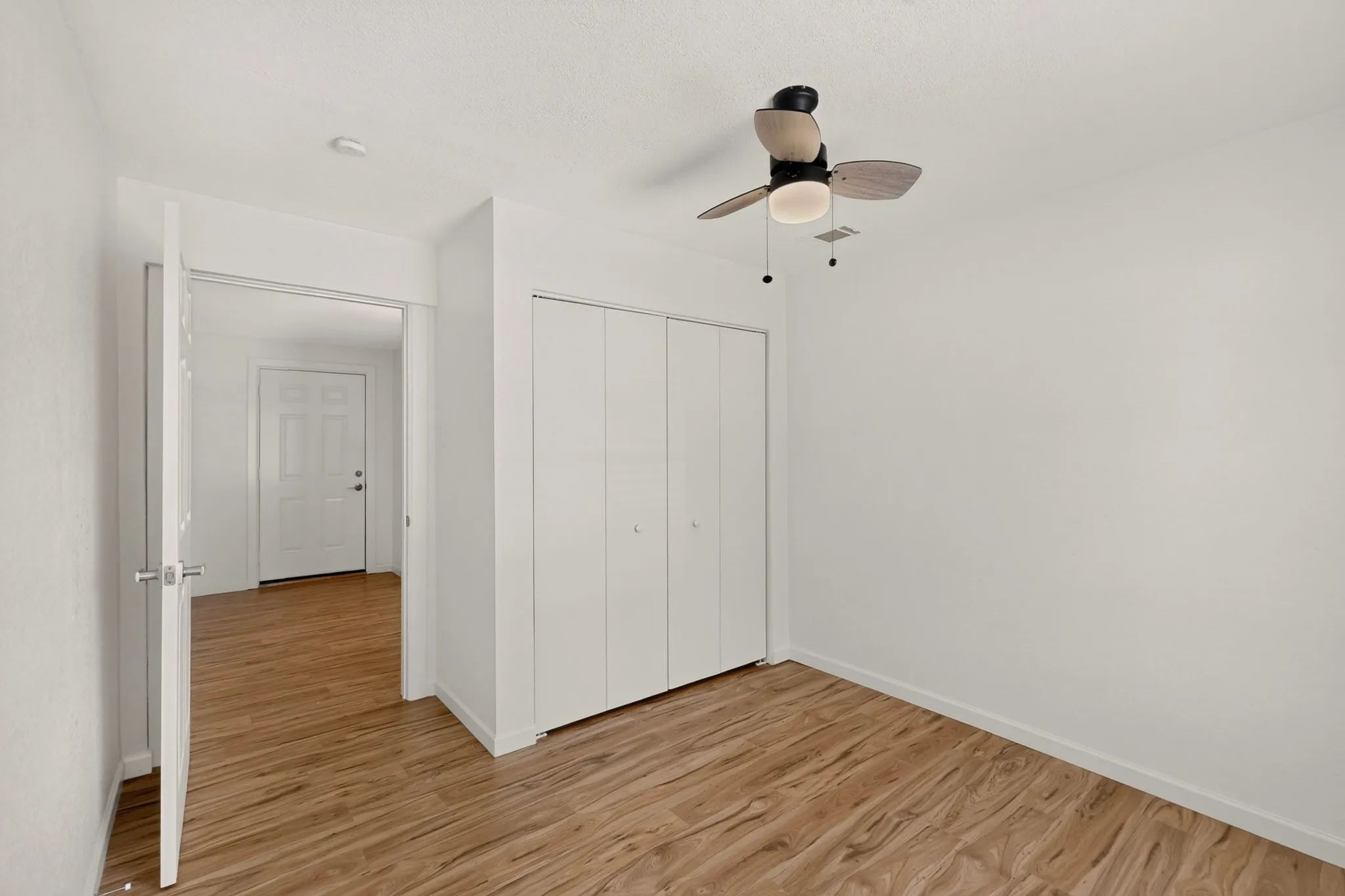 Room featuring wood-finish flooring, a ceiling fan with integrated lighting, and a double-door closet