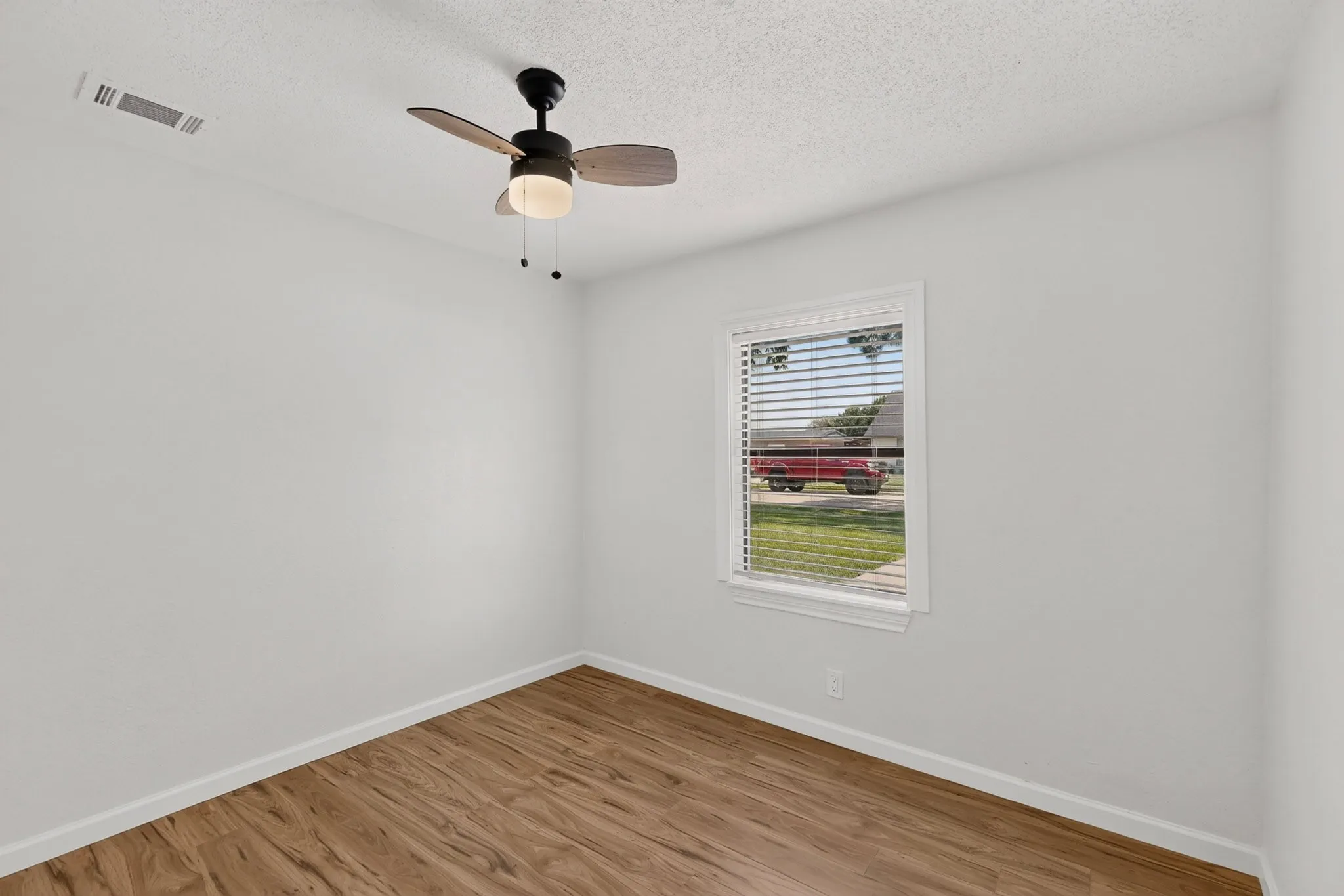 Room featuring wood-finish flooring, white painted walls, and a ceiling fan with integrated lighting