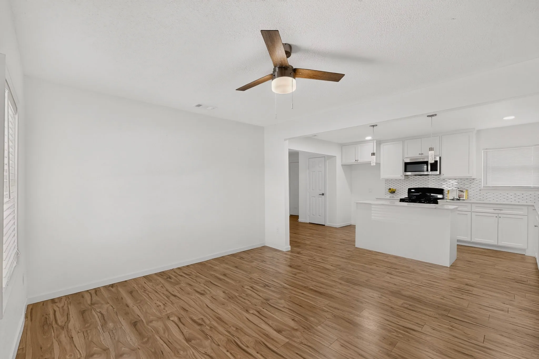 Bright open-concept living area featuring wood-finish flooring and a contemporary ceiling fan