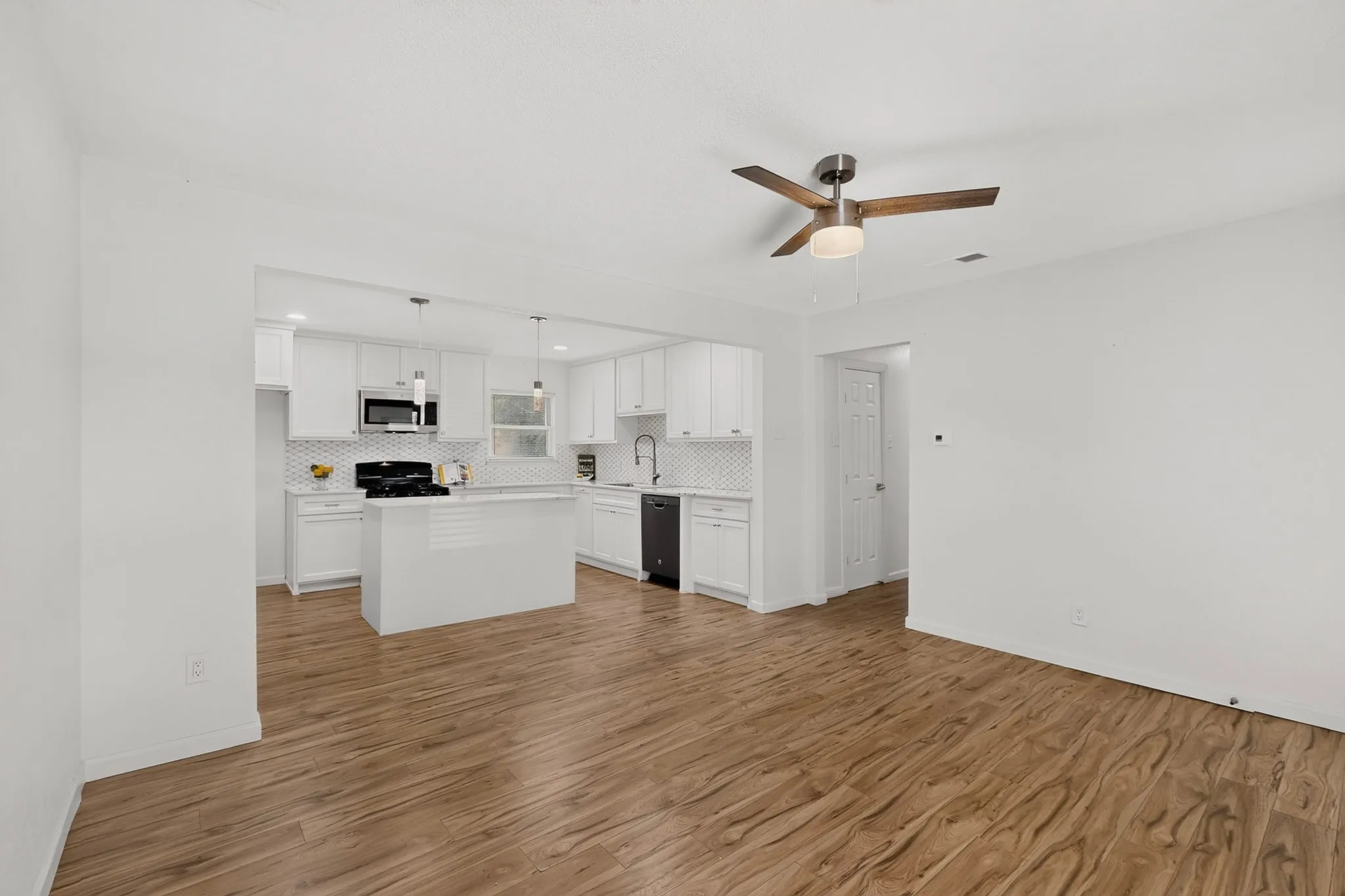 Spacious open-concept area featuring wood-finish flooring, a contemporary ceiling fan, and crisp white walls