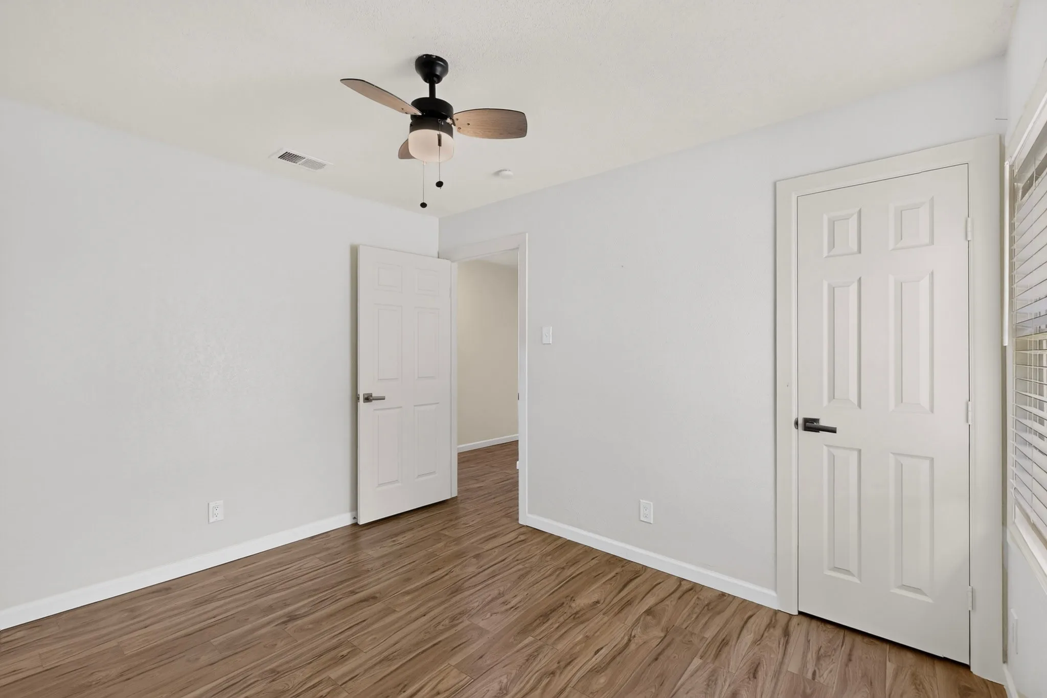 Interior room featuring wood-finish flooring, white painted walls, and a ceiling fan with integrated lighting