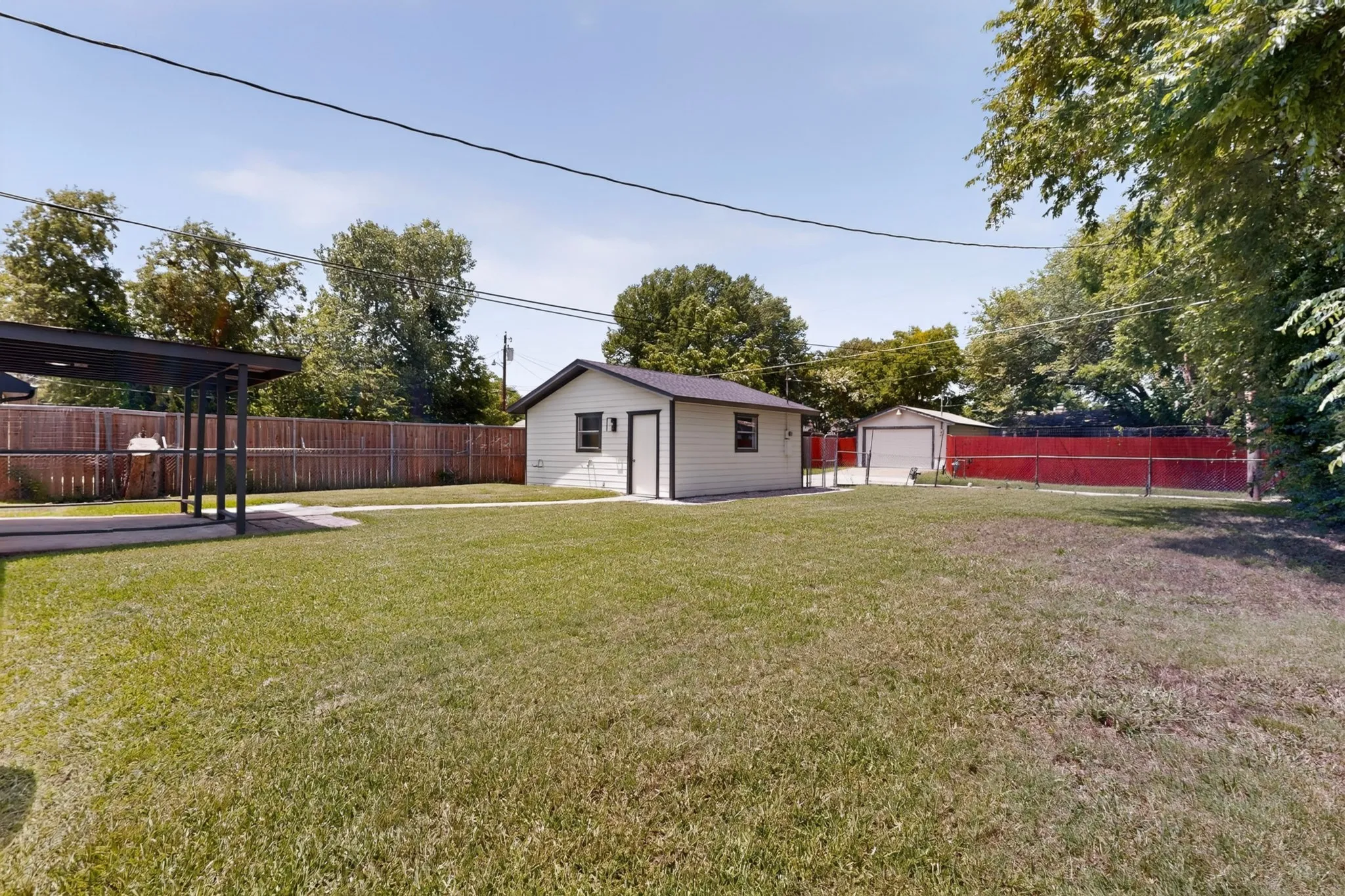 Expansive green lawn featuring a detached accessory structure, separate garage, perimeter fencing, and covered patio