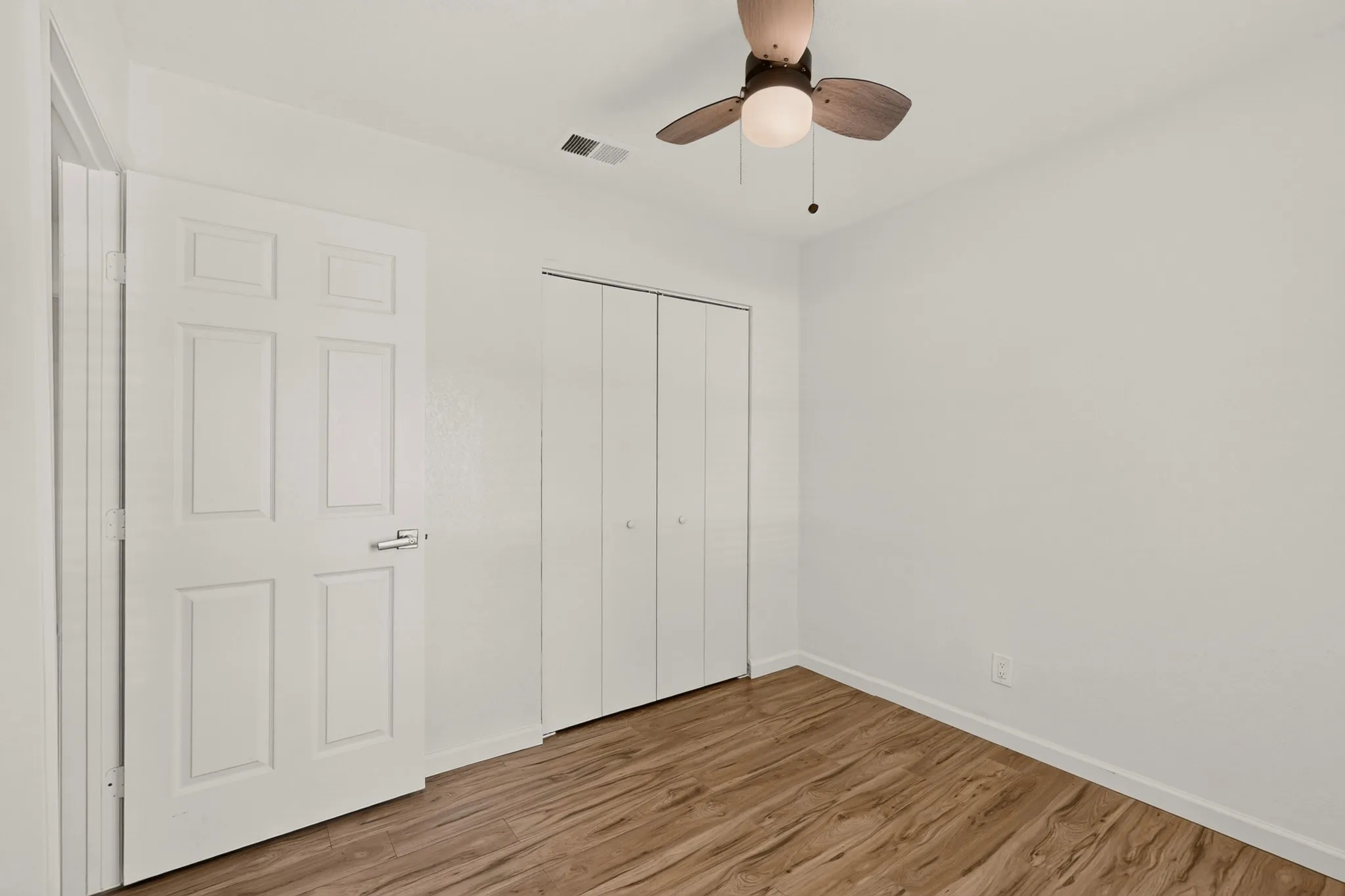Spacious room with wood-finish flooring and a ceiling fan