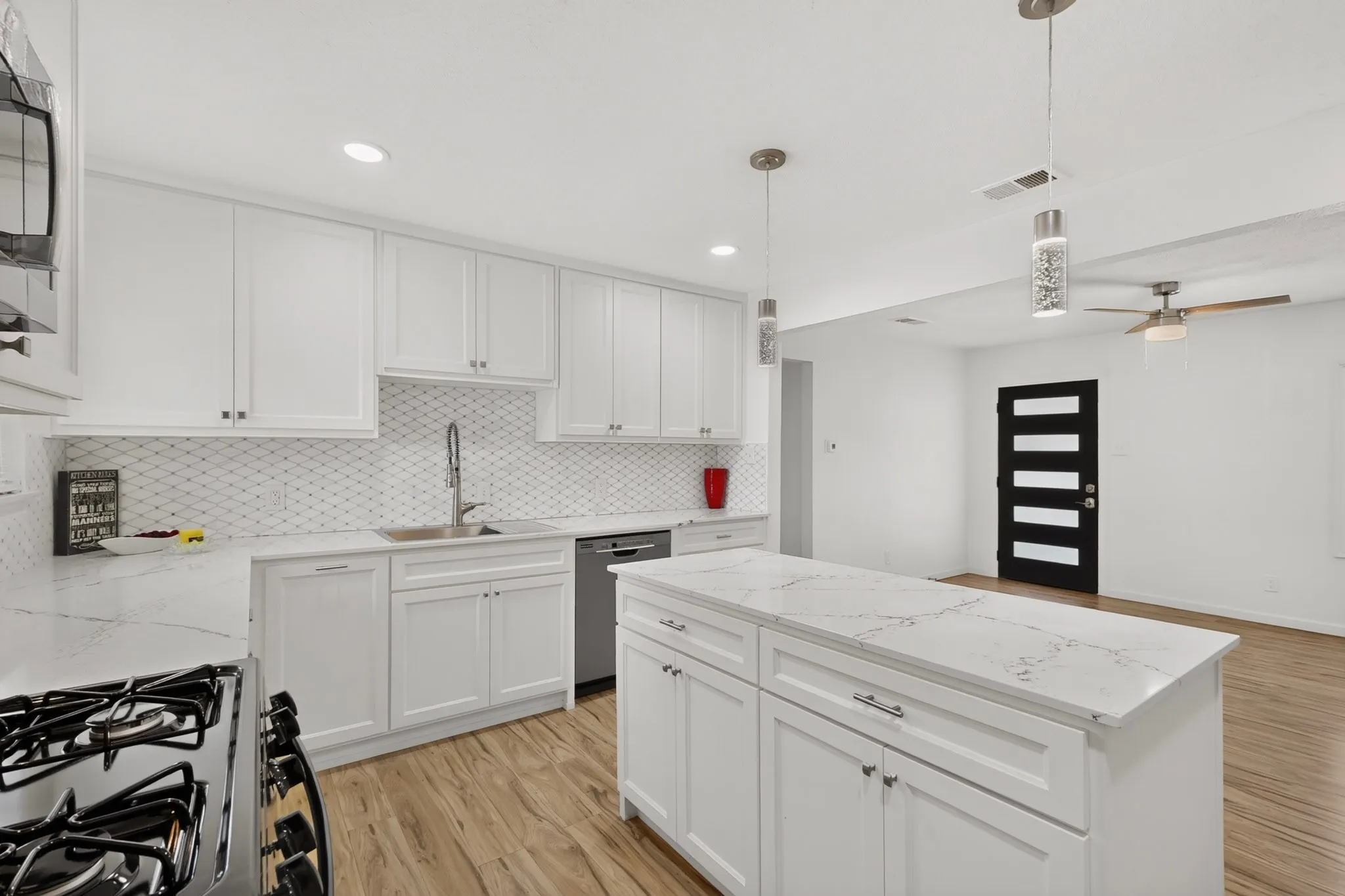 Modern kitchen featuring white cabinetry, light-toned countertops, a stainless steel sink, a geometric tile backsplash, and recessed lighting