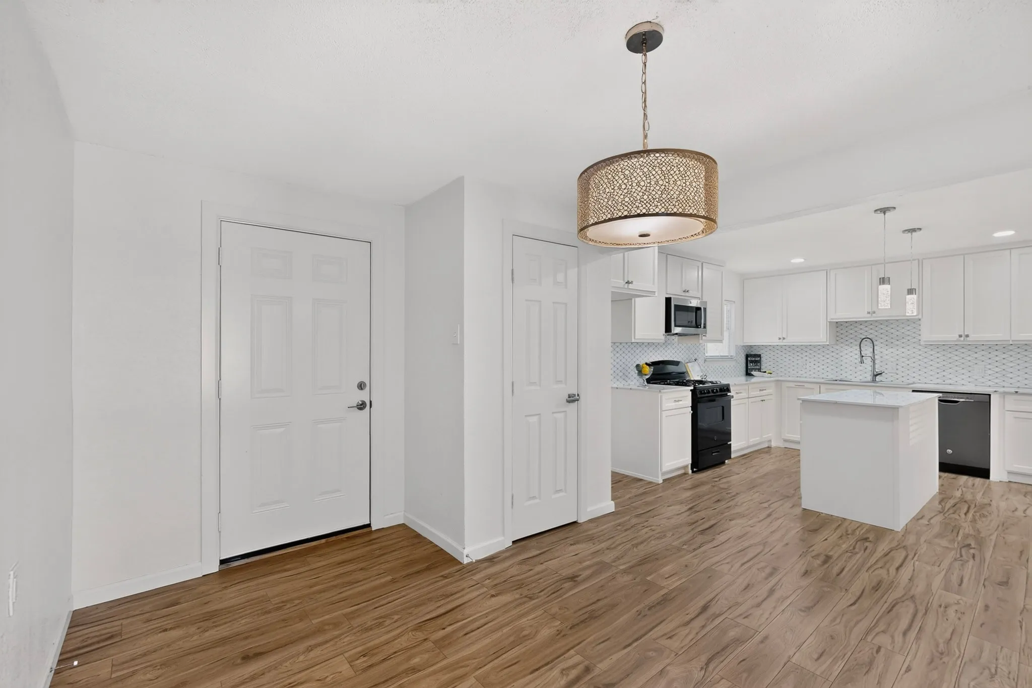 Open-concept kitchen featuring wood-finish flooring, white cabinetry, a central island, and a tiled backsplash
