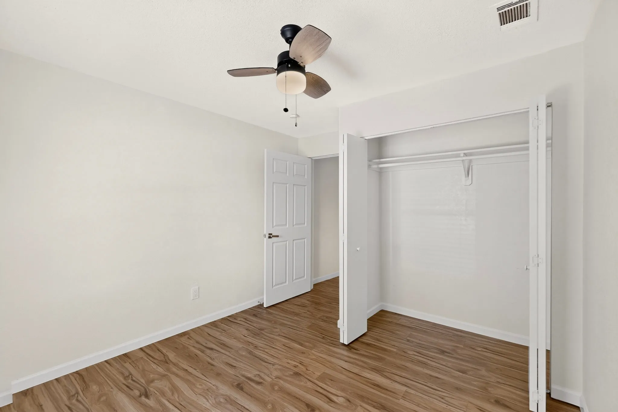 Interior room featuring wood-finish flooring, white walls, and a ceiling fan with integrated lighting