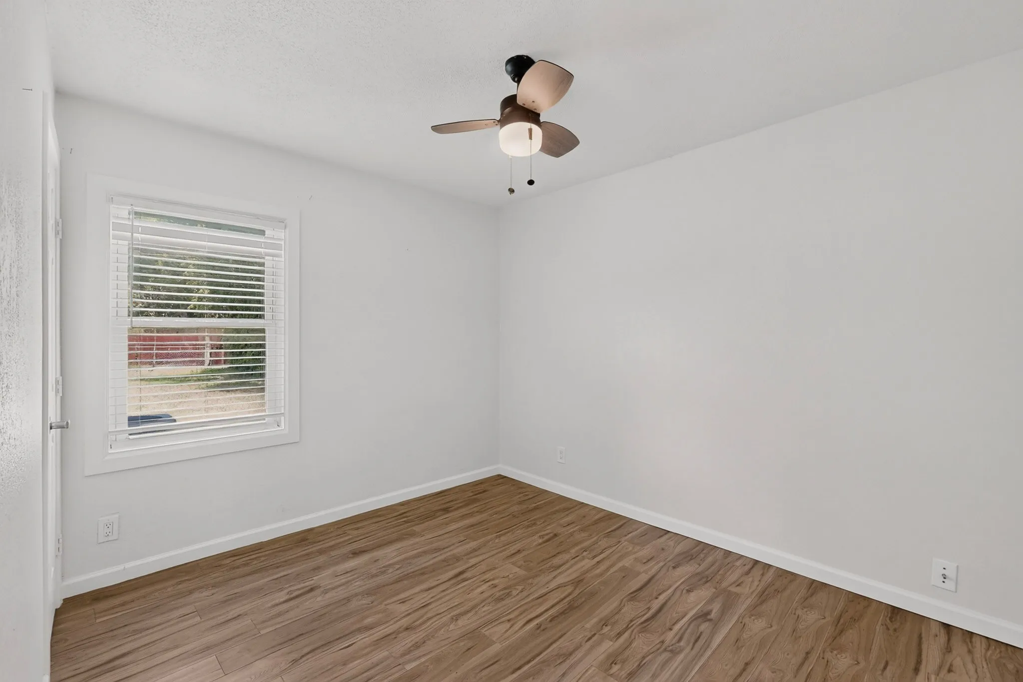 Spacious room featuring wood-finish flooring, a window with blinds, and a ceiling fan with integrated lighting