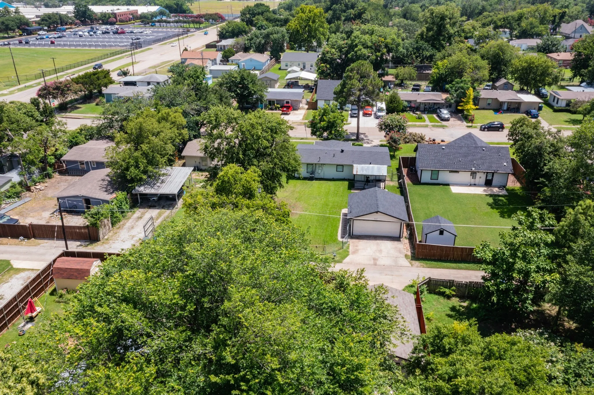 Rear exterior featuring a spacious fenced yard, detached garage with driveway, and a white storage shed