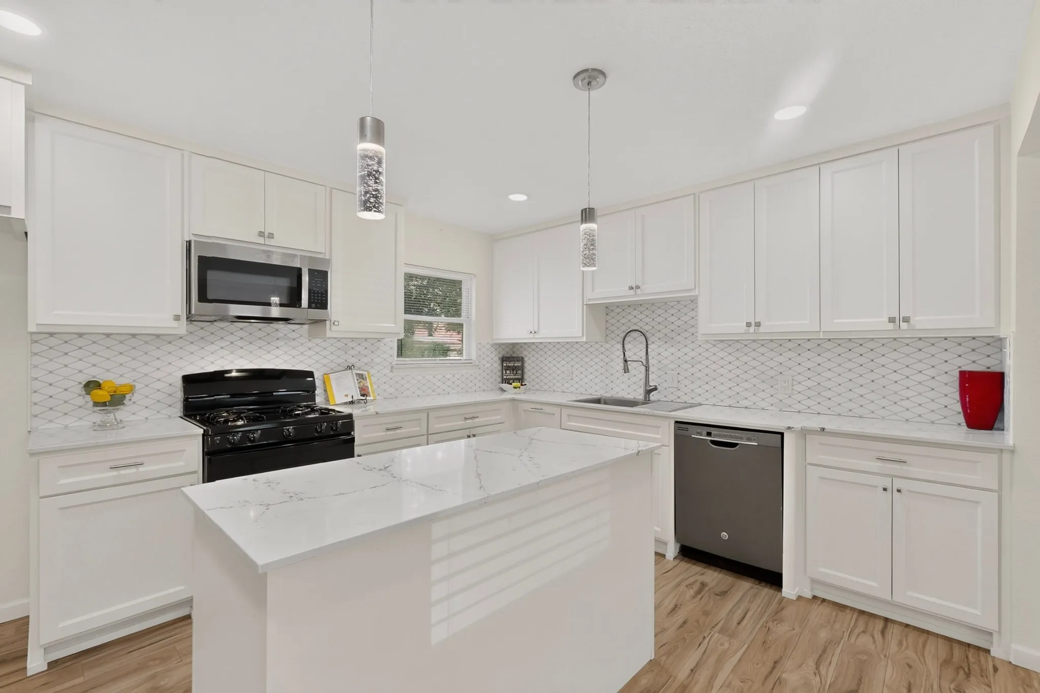 Modern kitchen featuring a central island with a stone-finish countertop, white cabinetry, stainless steel appliances, decorative tiled backsplash, and wood-finish flooring