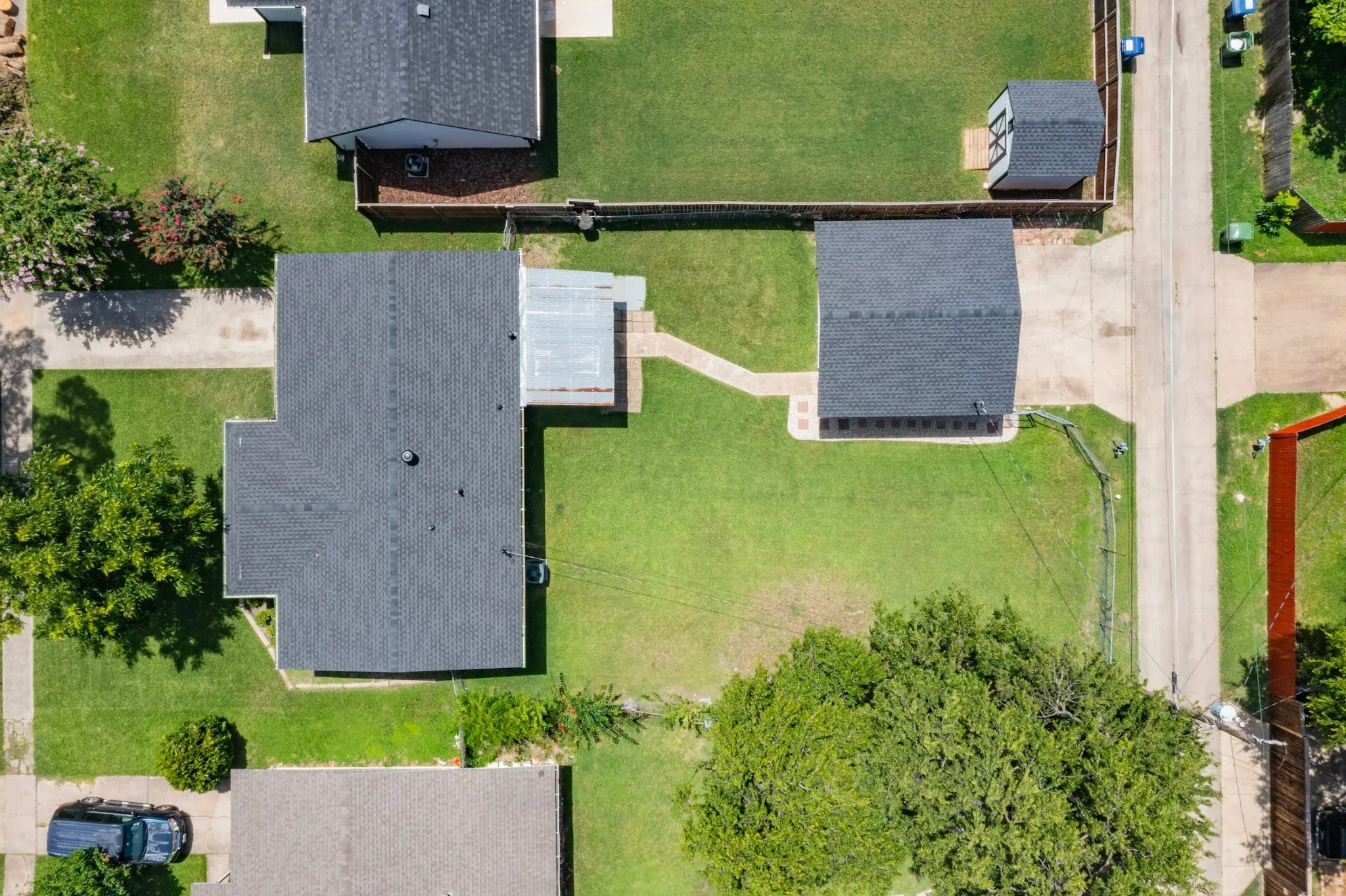 Expansive property featuring a main residence with a dark shingle roof, a detached garage with a dark shingle roof, a covered patio area, and a separate storage shed