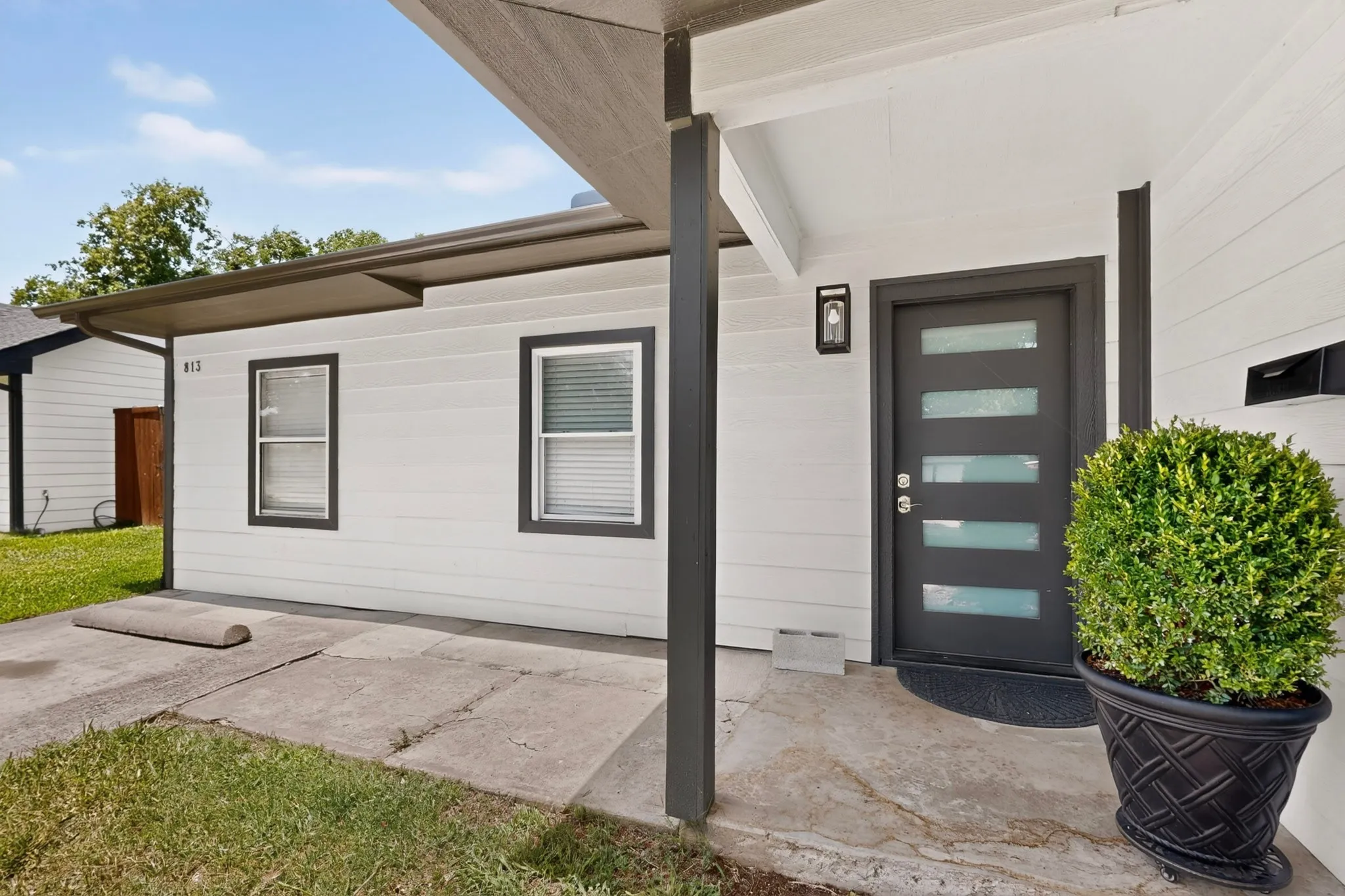 Modern entry featuring a dark gray door with frosted glass panels, an exterior wall sconce, and a matching dark gray mailbox