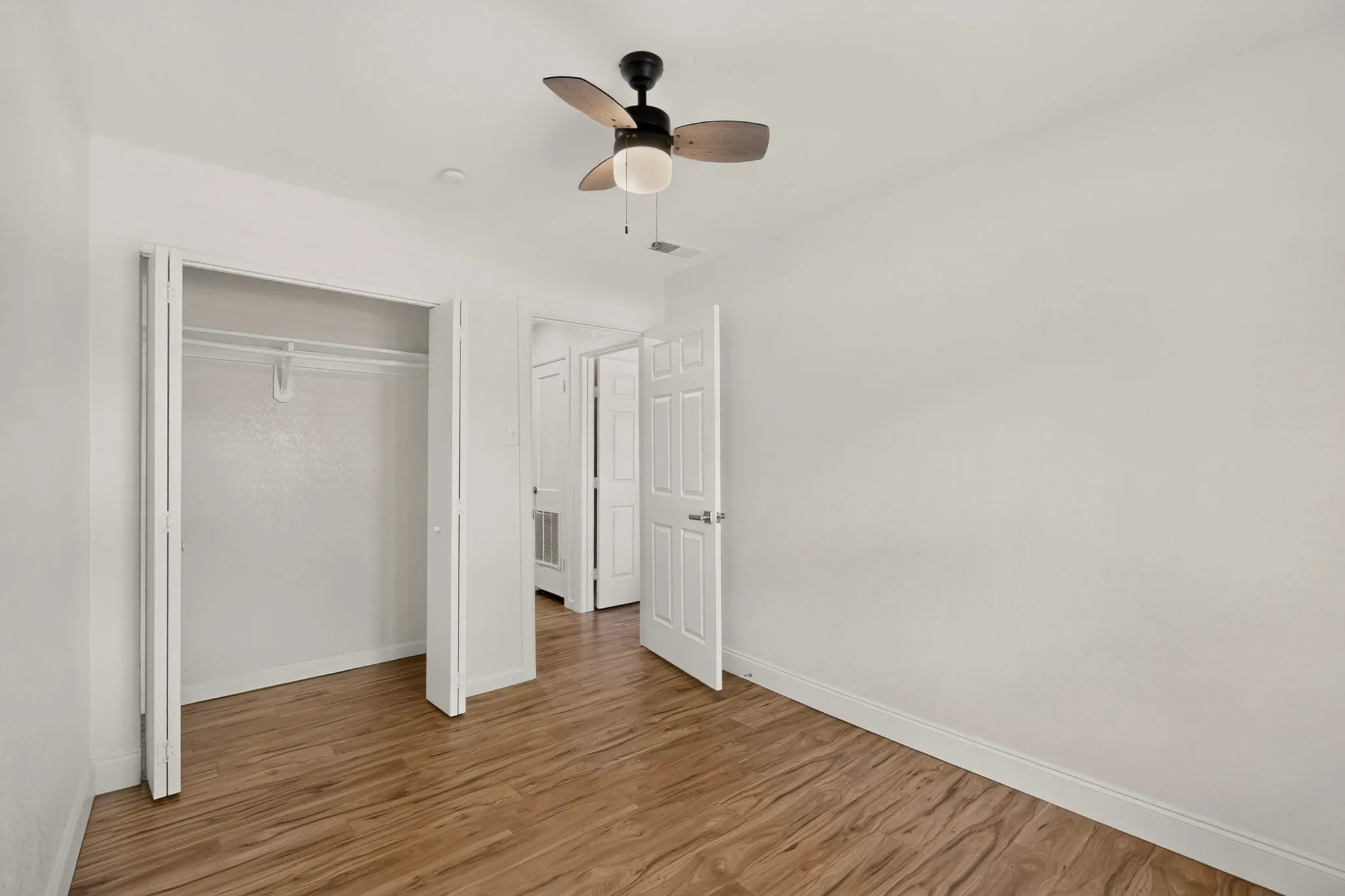 Spacious room featuring wood-finish flooring, crisp white walls, and a ceiling fan with integrated lighting