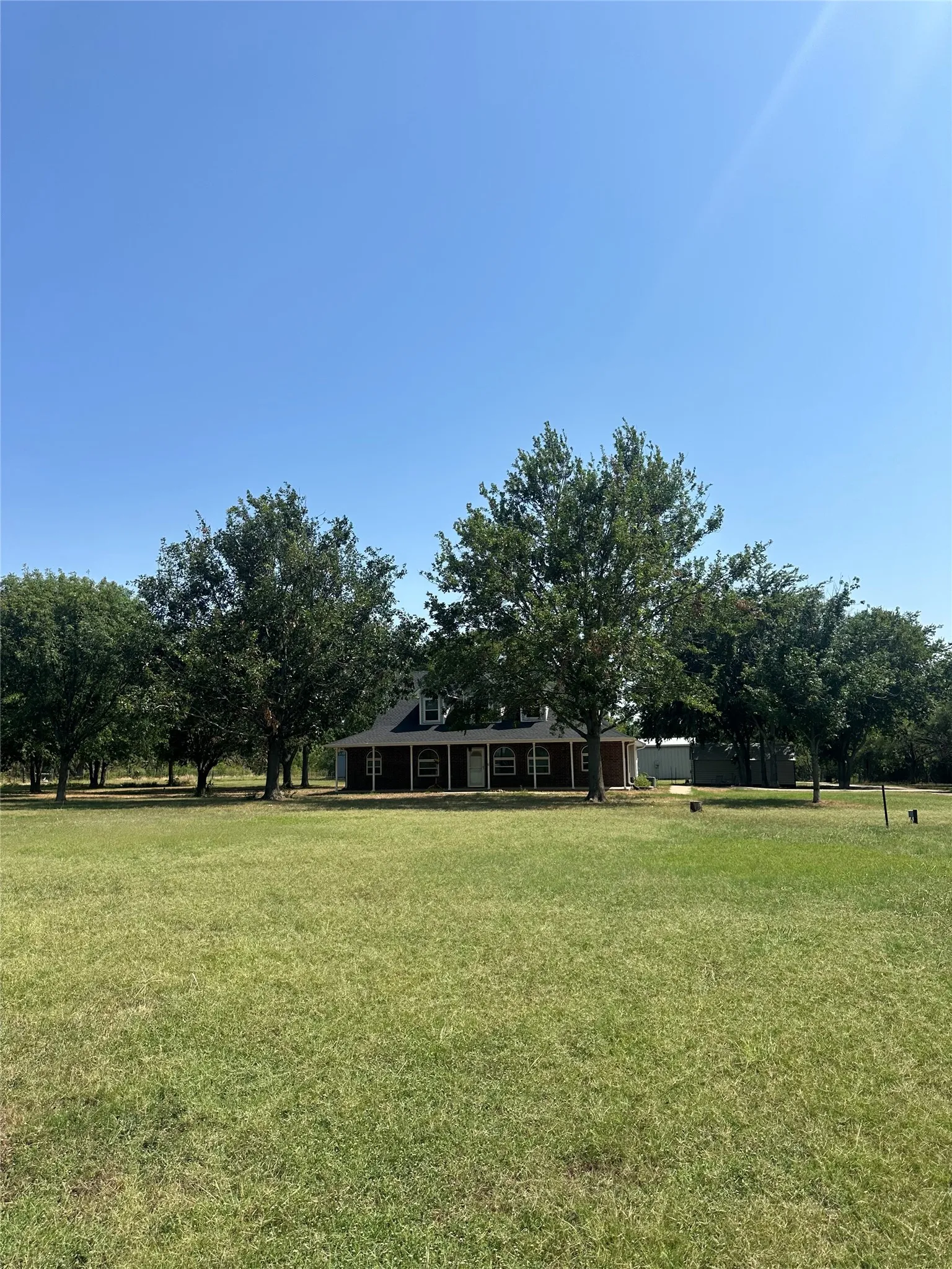 Sprawling lawn with mature trees and a dark-sided residence featuring white window trim