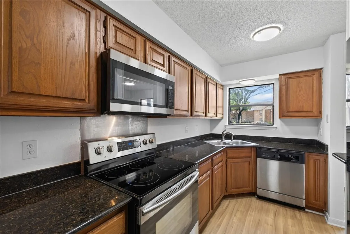 Kitchen featuring wood cabinetry, dark countertops, stainless steel appliances, and wood-finish flooring