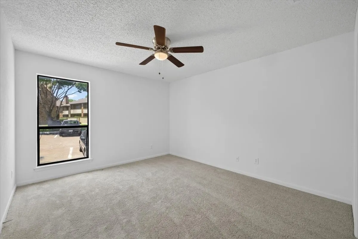 Carpeted Primary Bedoom featuring light carpeting, a textured white ceiling, and a ceiling fan with dark wood-finish blades with a single window, and a white closet door.