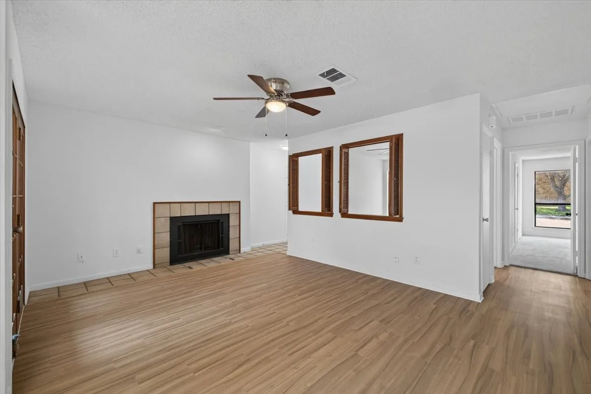 Spacious living area featuring wood-finish flooring, a tiled fireplace hearth, and a ceiling fan with integrated lighting