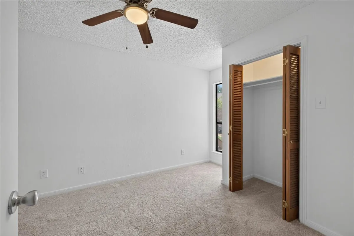 Spacious room featuring neutral carpeting, white walls, a ceiling fan with integrated lighting, a window, and bifold louvered closet doors