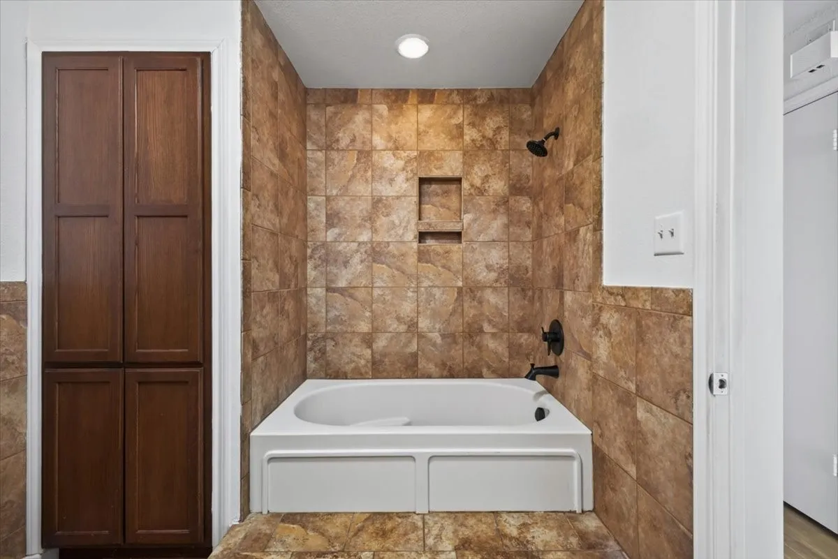 Bathtub with full-height wall tiling, recessed shower niche, and matte black fixtures