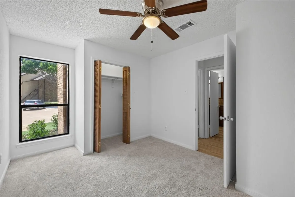 Carpeted room featuring a large window, bi-fold louvered closet doors, and a ceiling fan with light fixture