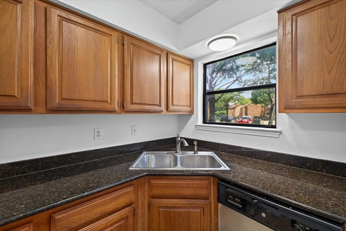 Kitchen featuring wood-finish cabinetry, dark speckled countertops, a double basin stainless steel sink with a chrome faucet, and a black dishwasher