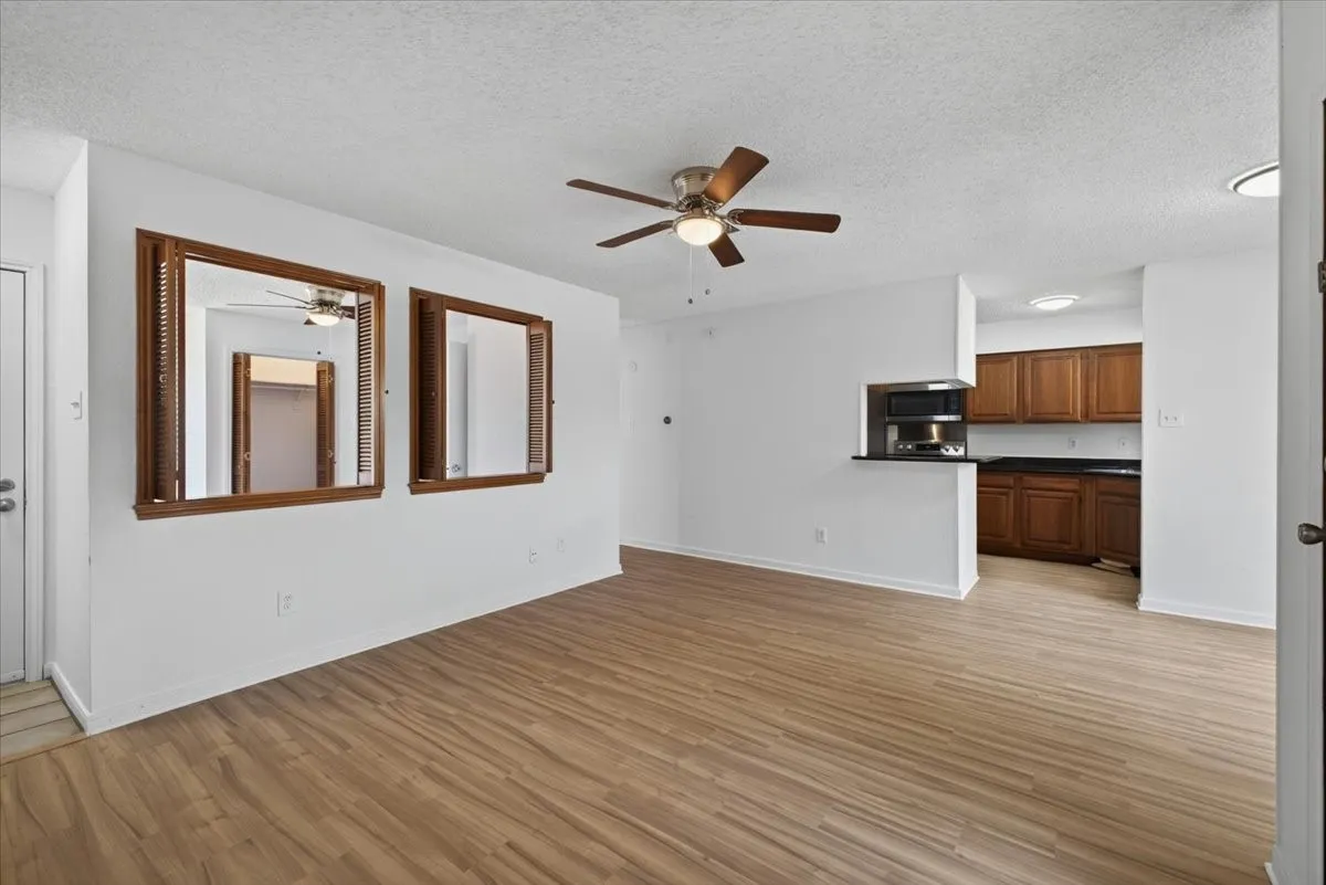Living area featuring wood-finish flooring, a ceiling fan with integrated lighting, and a pass-through opening to the kitchen