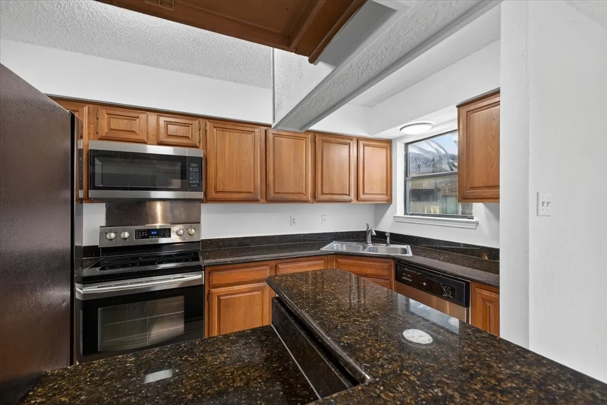 Kitchen featuring rich wood cabinetry, dark granite-style countertops, and stainless steel appliances including a built-in microwave, range, and dishwasher