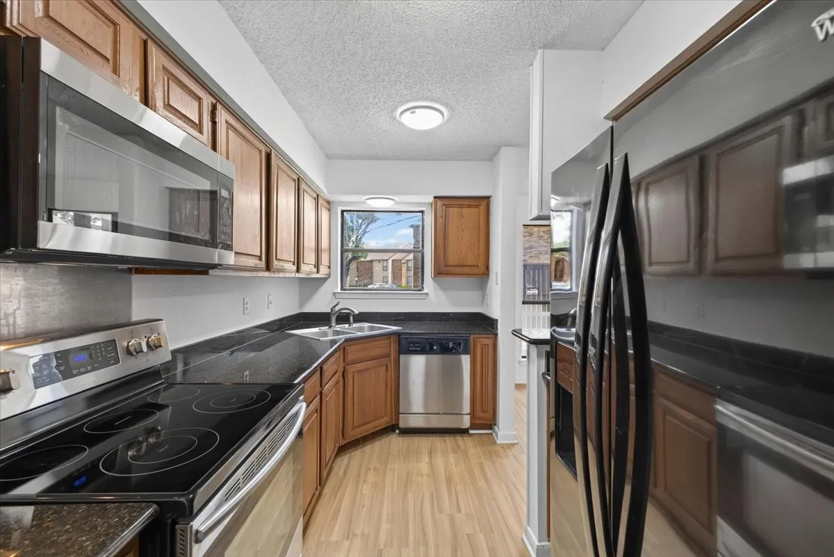 Kitchen featuring wood cabinetry, stainless steel appliances, dark countertops, and wood-finish flooring