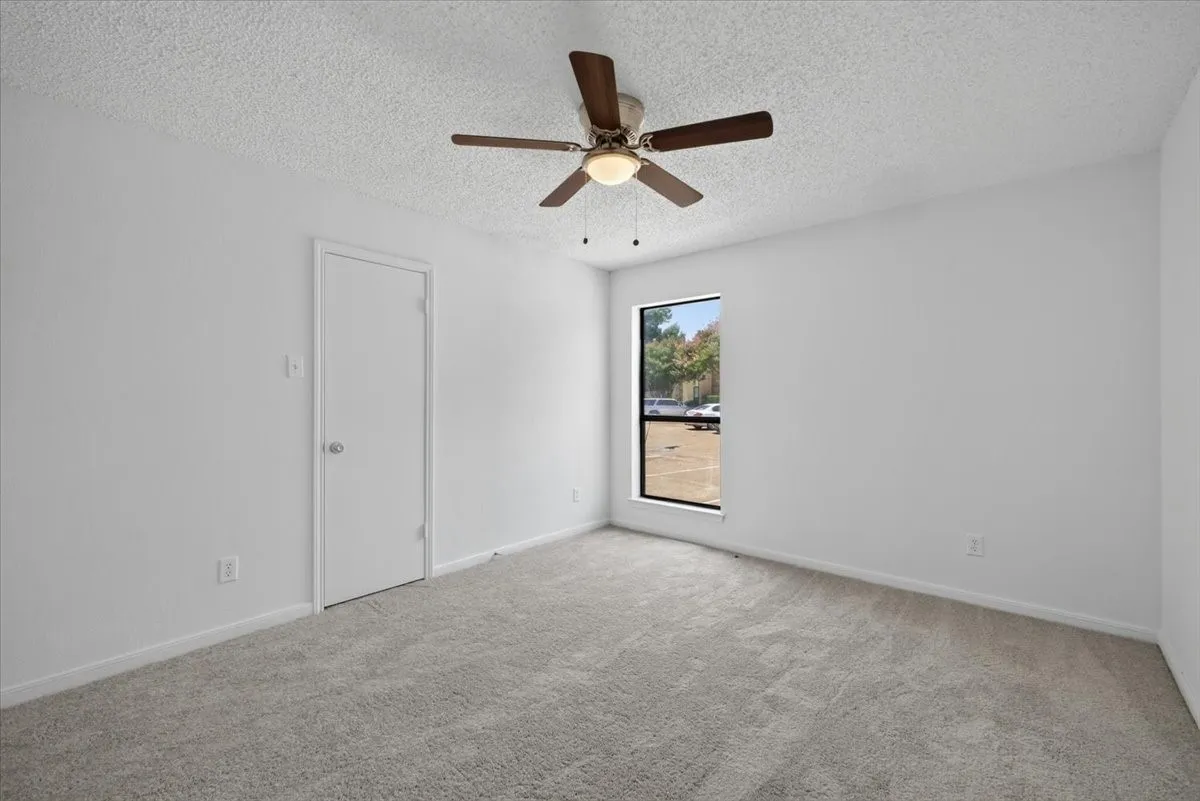 Carpeted Primary Bedoom featuring neutral carpeting, a textured white ceiling, and a ceiling fan with dark wood-finish blades with a single window, and a white closet door.