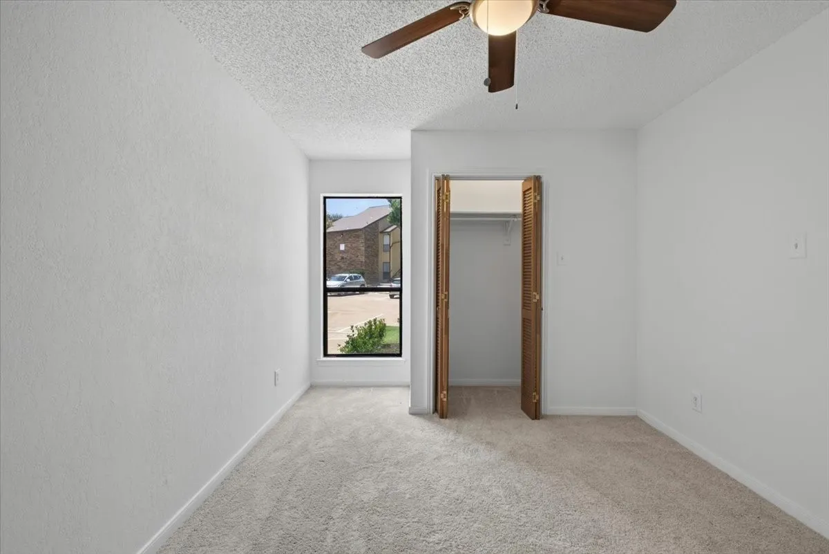 Carpeted interior space with a ceiling fan, a window, and a closet with bifold doors