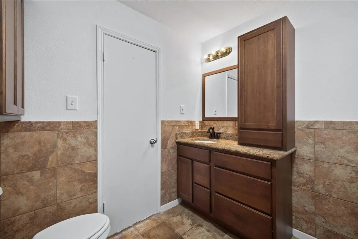 Bathroom featuring a wood-finish vanity with a granite countertop, undermount sink, and bronze-finish faucet