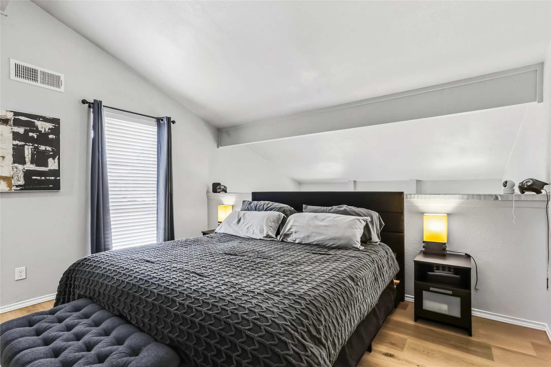 Vaulted ceiling bedroom featuring wood-finish flooring, a window with horizontal blinds, and a built-in wall shelf