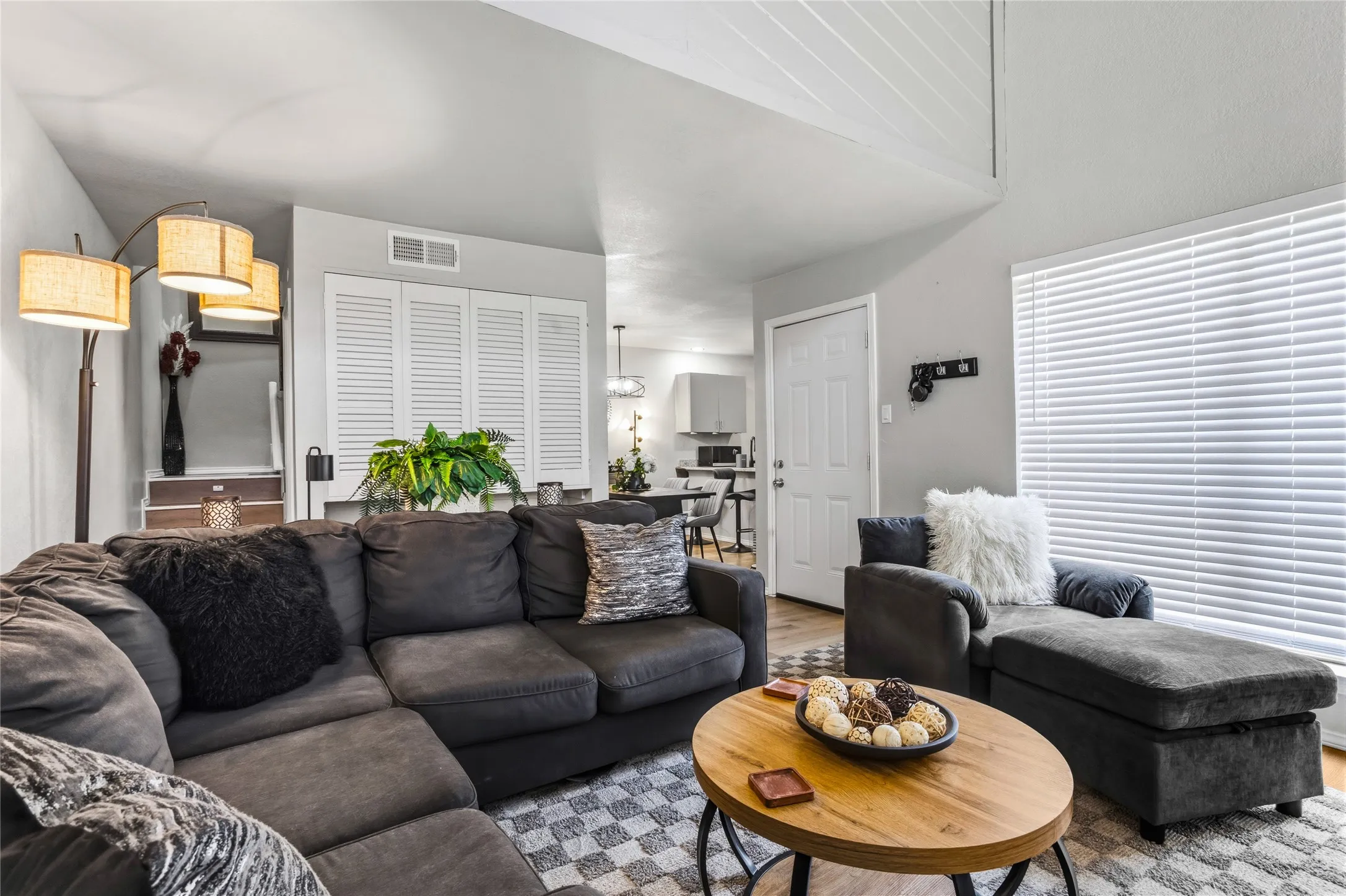 Living area featuring vaulted ceilings, wood-finish flooring, and white louvered bifold doors for storage and a space underneath for a kennel if needed.