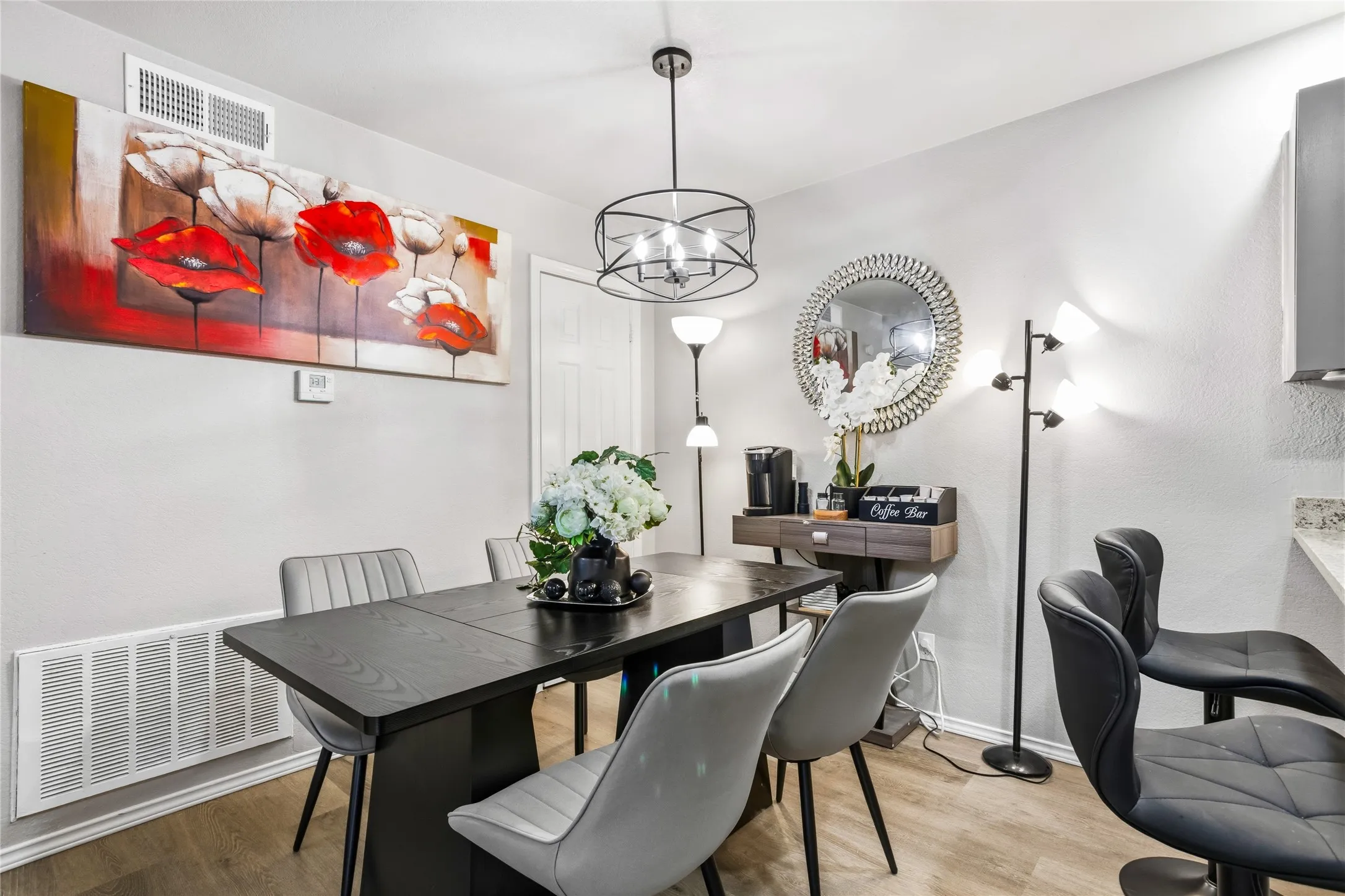 Dining area featuring wood-finish flooring, a contemporary black chandelier, a built-in wall vent, and light-colored walls