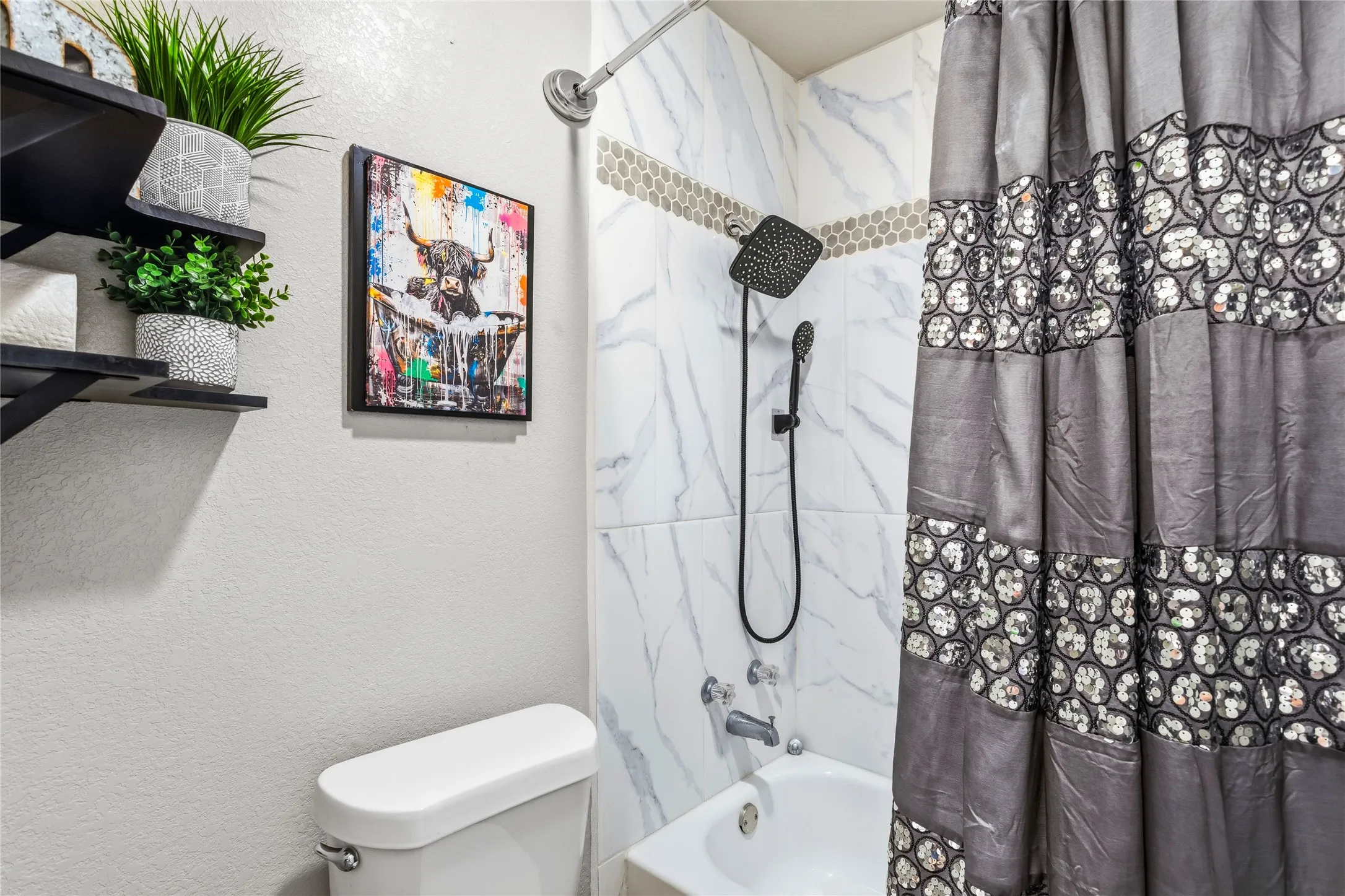 Bathtub shower combination featuring white marble-patterned tile, a mosaic tile accent band, and black shower fixtures