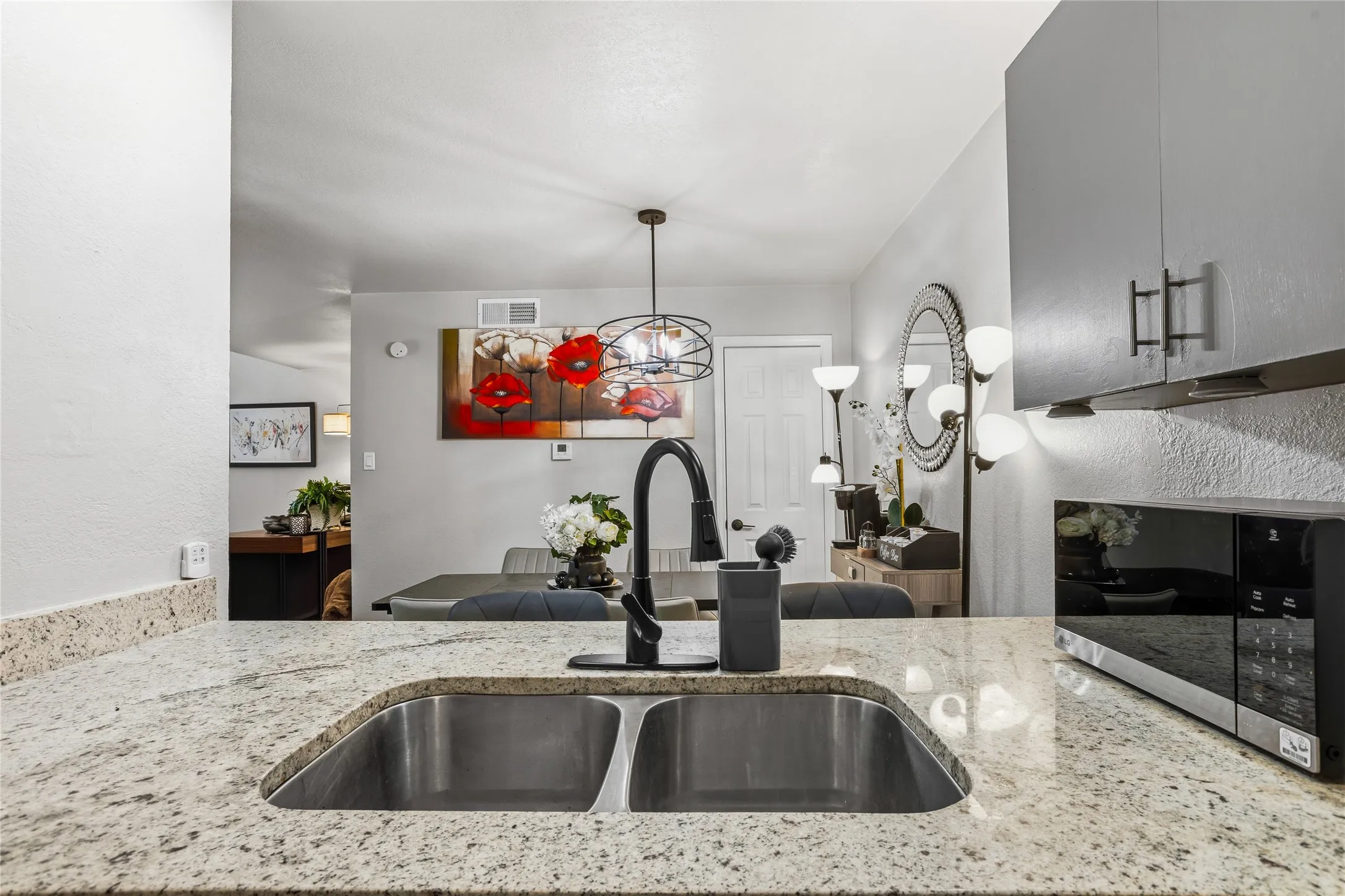 Kitchen featuring light-toned countertops, a dual basin stainless steel sink with a matte black faucet, and an integrated microwave