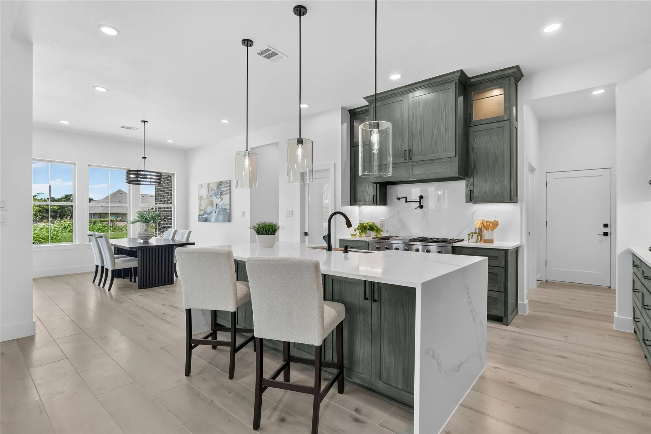 Open-concept kitchen and dining area featuring a waterfall-edge island with seating, a gas range with a tile backsplash, wood-finish flooring, and ample natural light from multiple windows