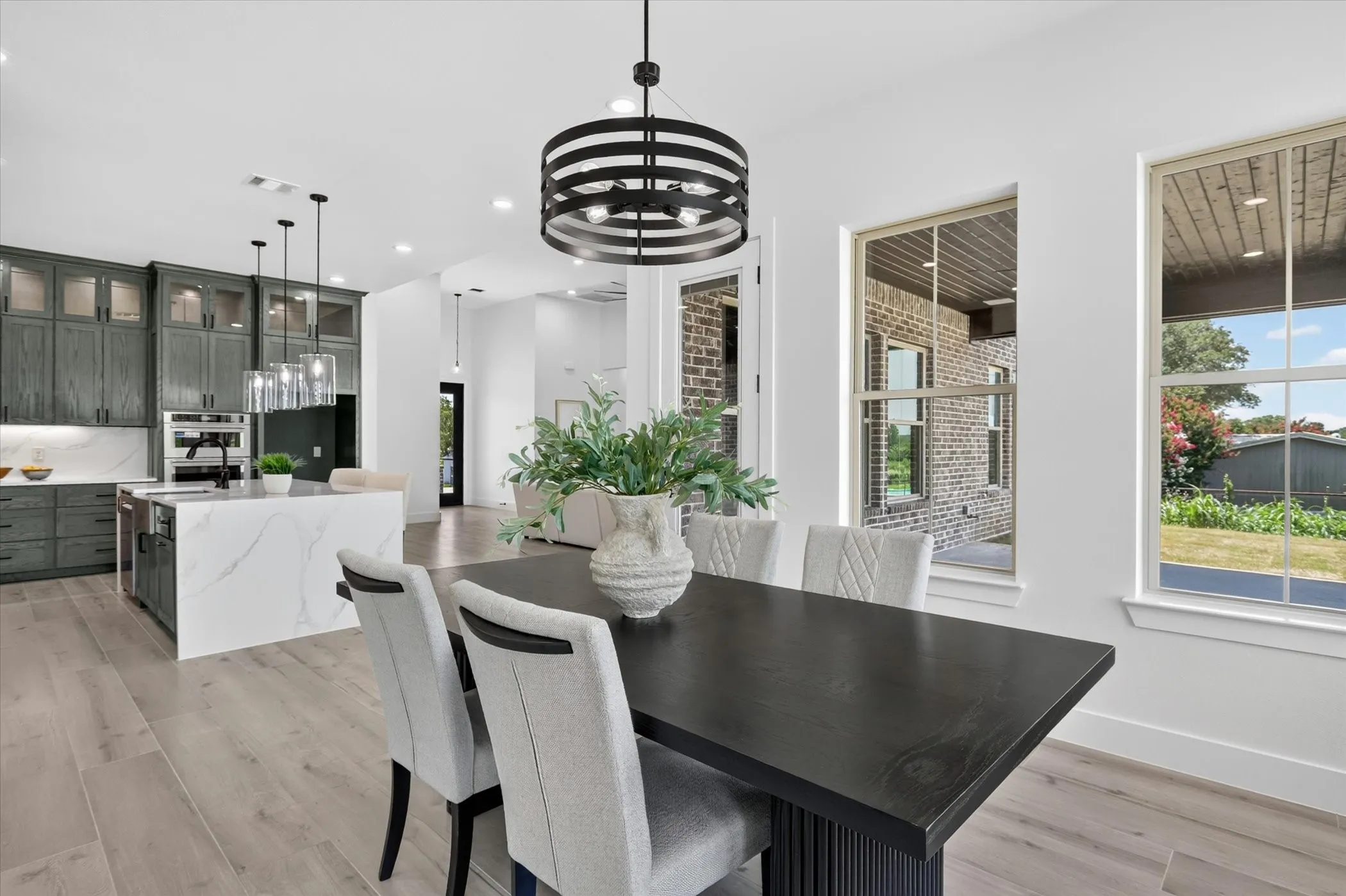 Open-concept dining area with wood-finish flooring, a modern black chandelier, and expansive windows