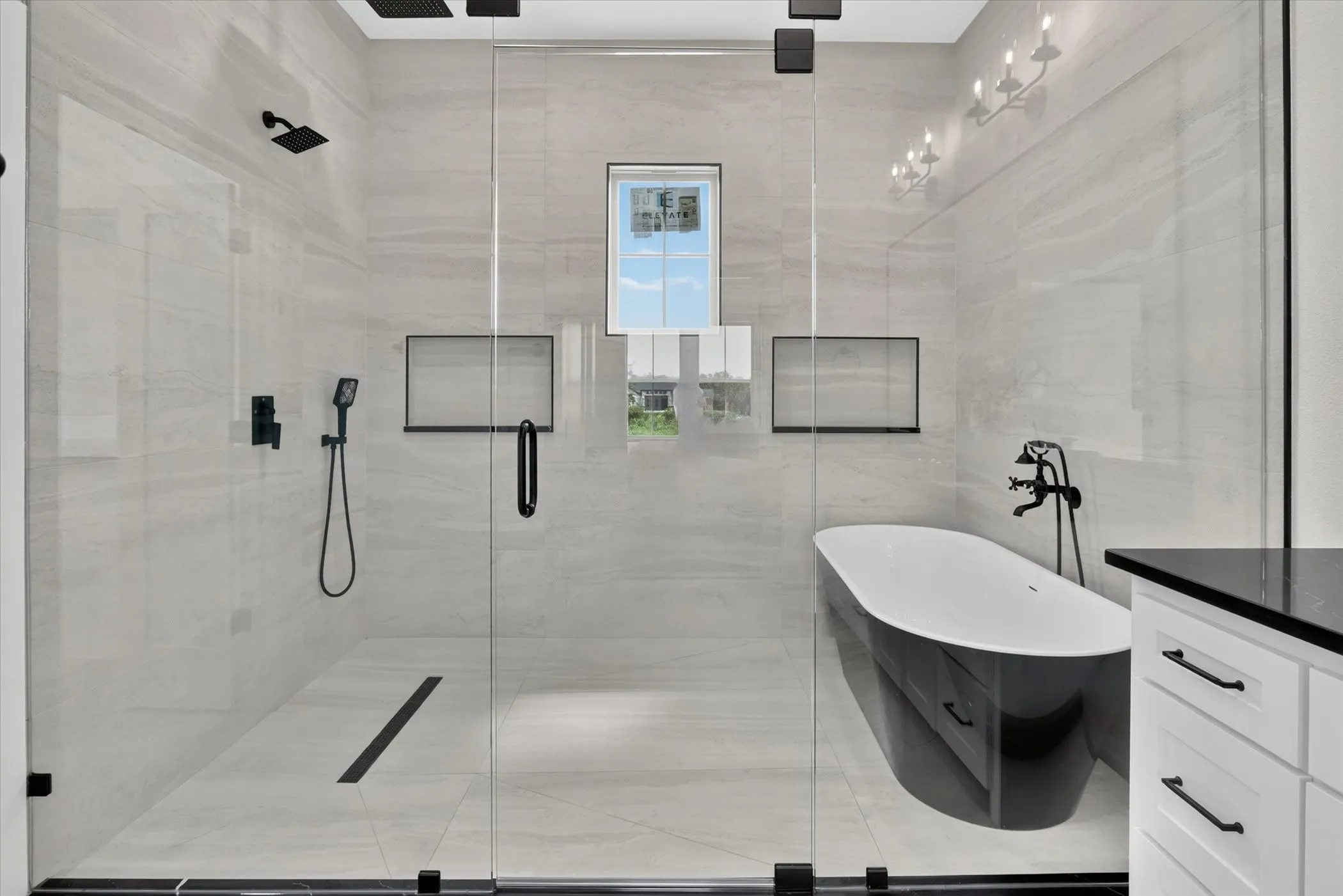 Glass-enclosed shower with matte black fixtures, integrated linear drain, and dual showerheads