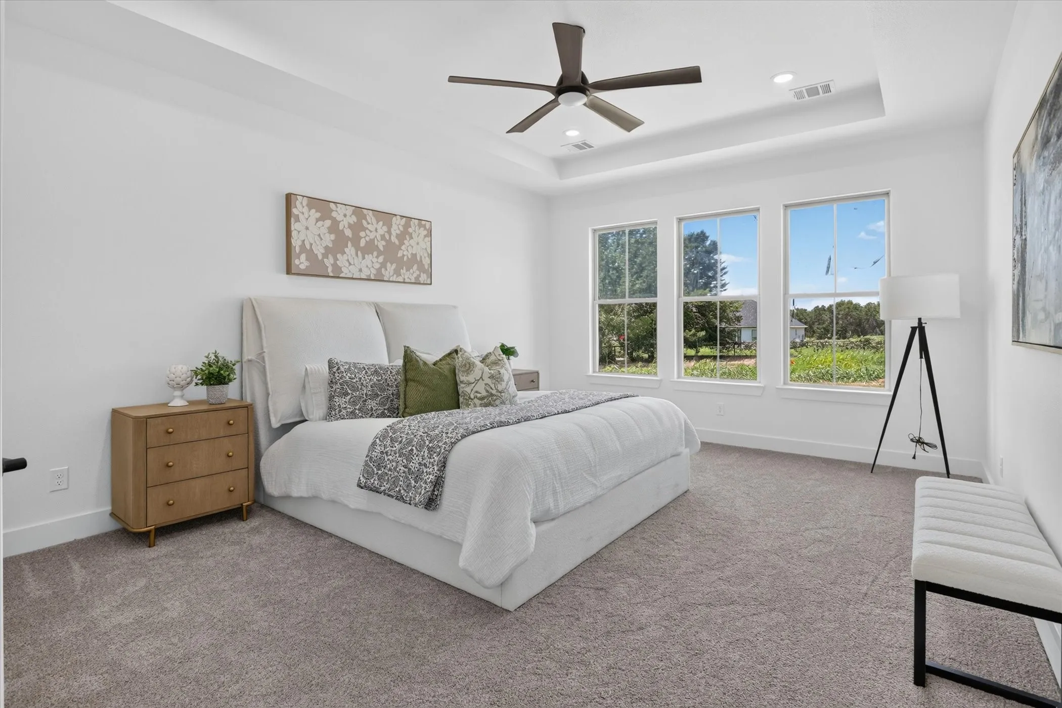 Spacious bedroom featuring a tray ceiling, ceiling fan, triple windows, and neutral carpeting