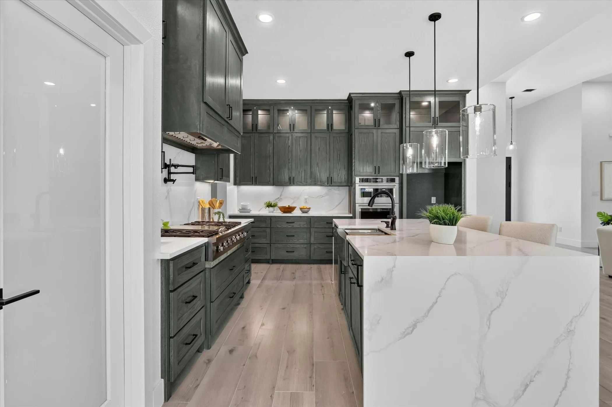 Gourmet kitchen featuring a waterfall island with stone countertop, dark wood-finish cabinetry, stainless steel appliances, and pendant lighting