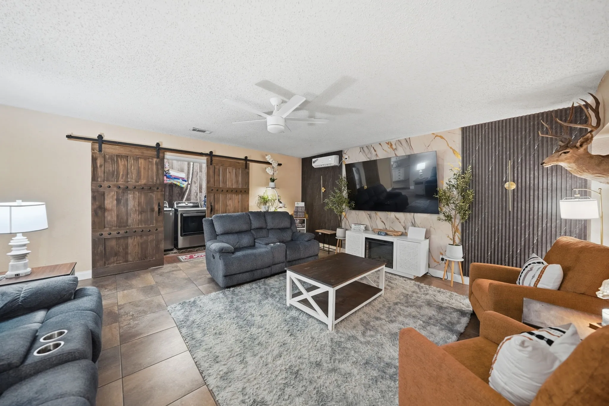 Living area featuring tile flooring, a ceiling fan, and a decorative accent wall with vertical paneling