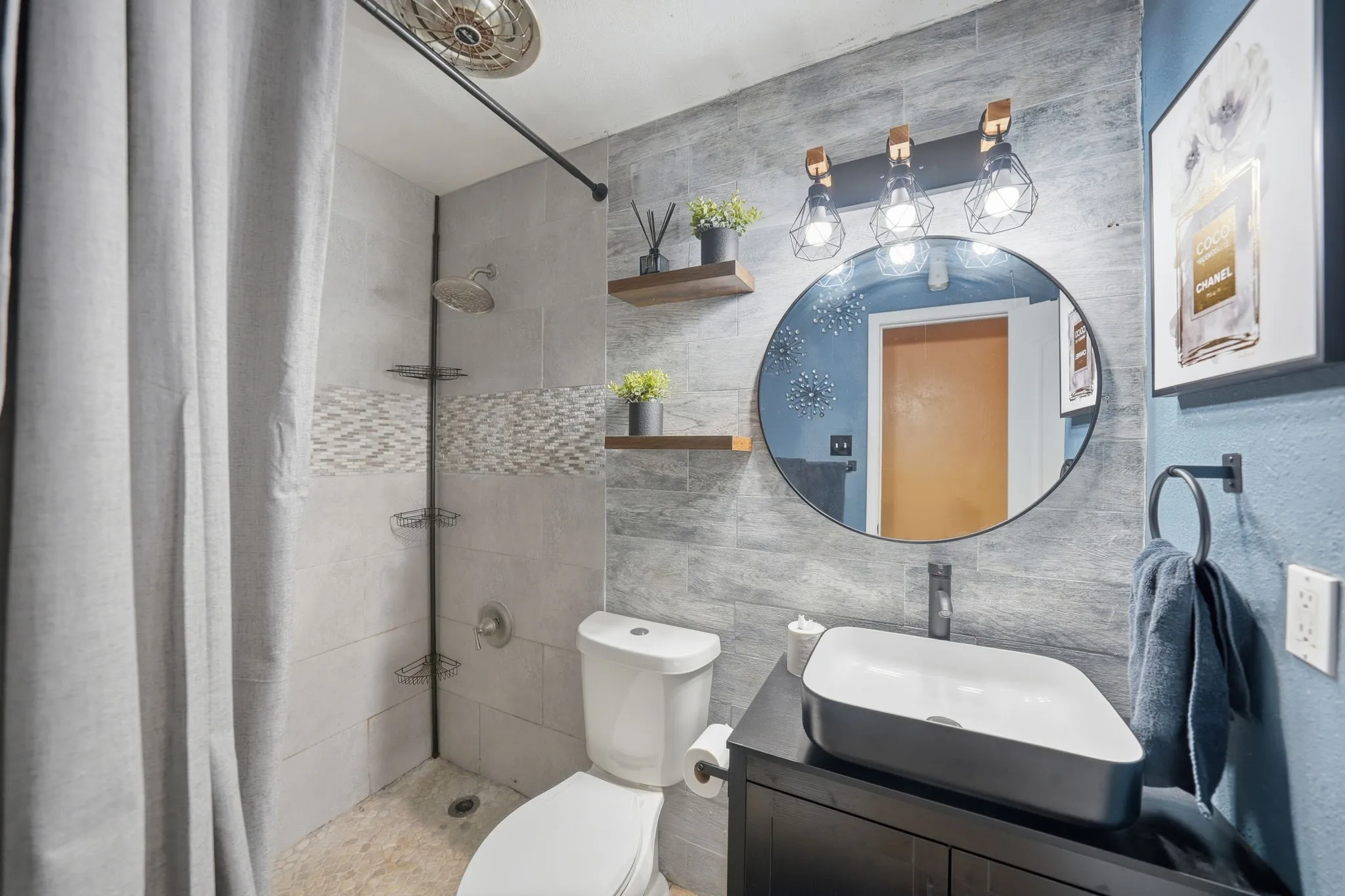 Bathroom featuring a vessel sink with a black vanity, round mirror, and industrial-style lighting