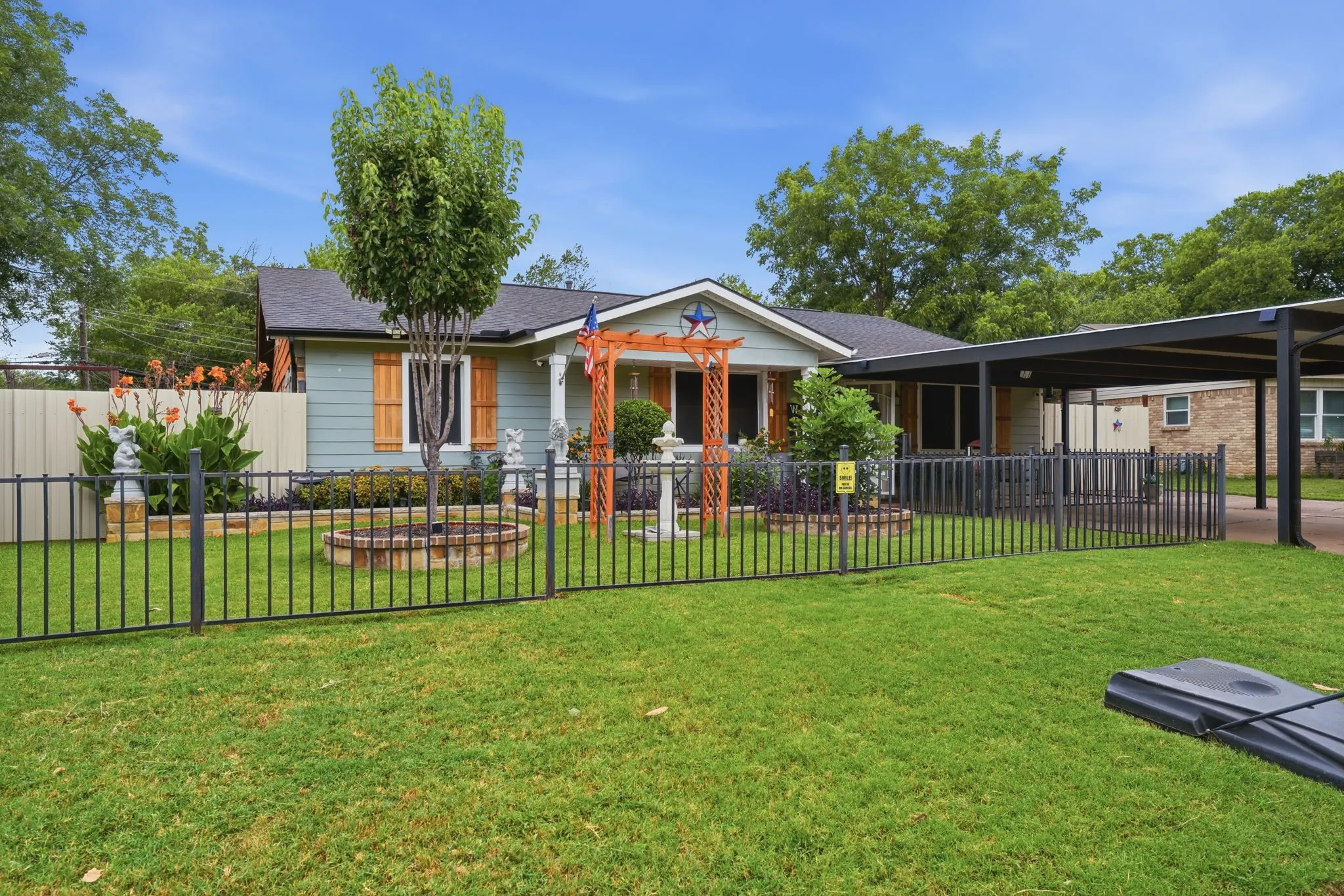 Front exterior featuring light blue siding, black shingle roof, and a black metal fence
