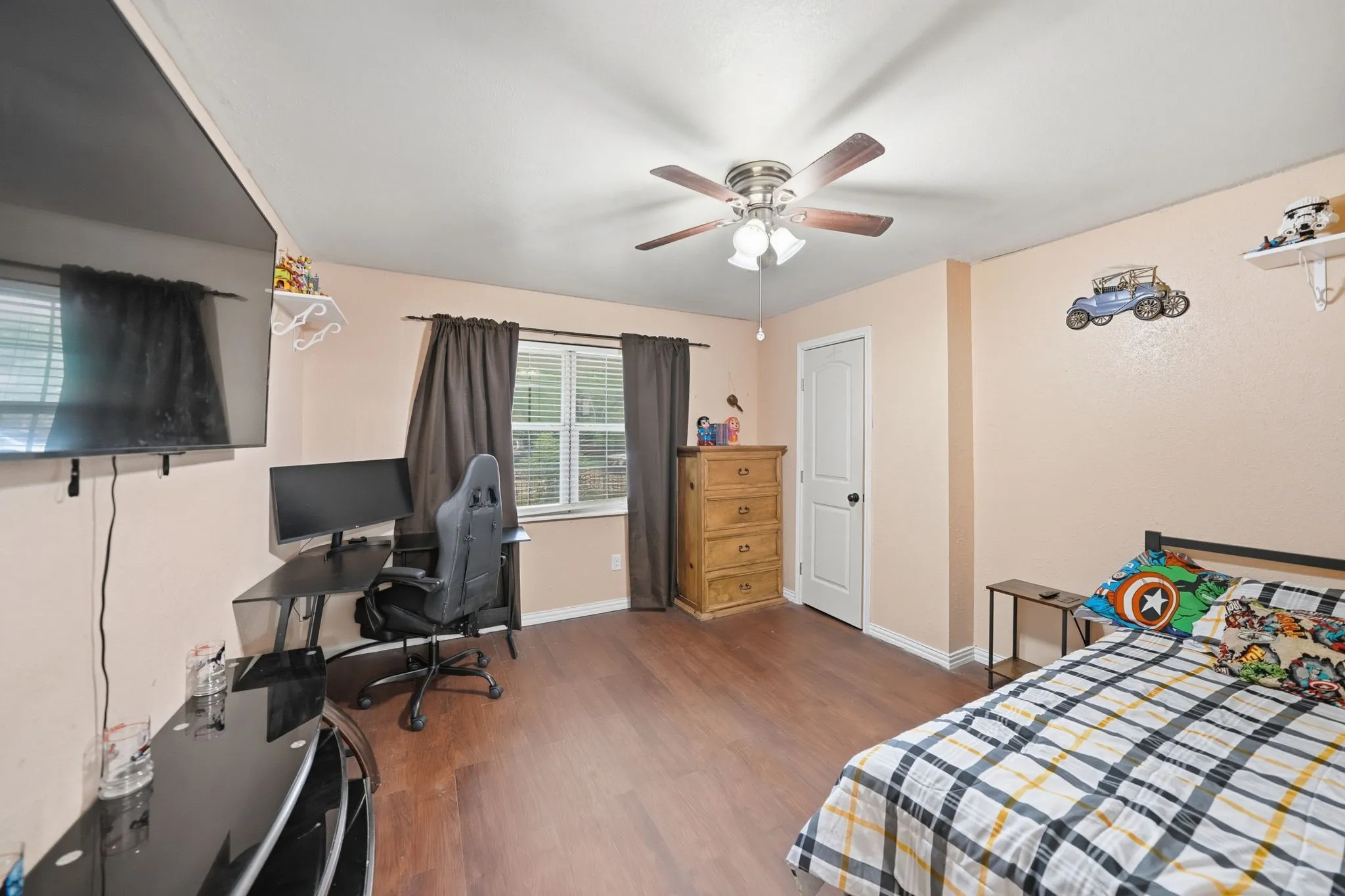 Bedroom featuring wood-finish flooring, a ceiling fan with integrated lighting, and a window with blinds and dark curtains
