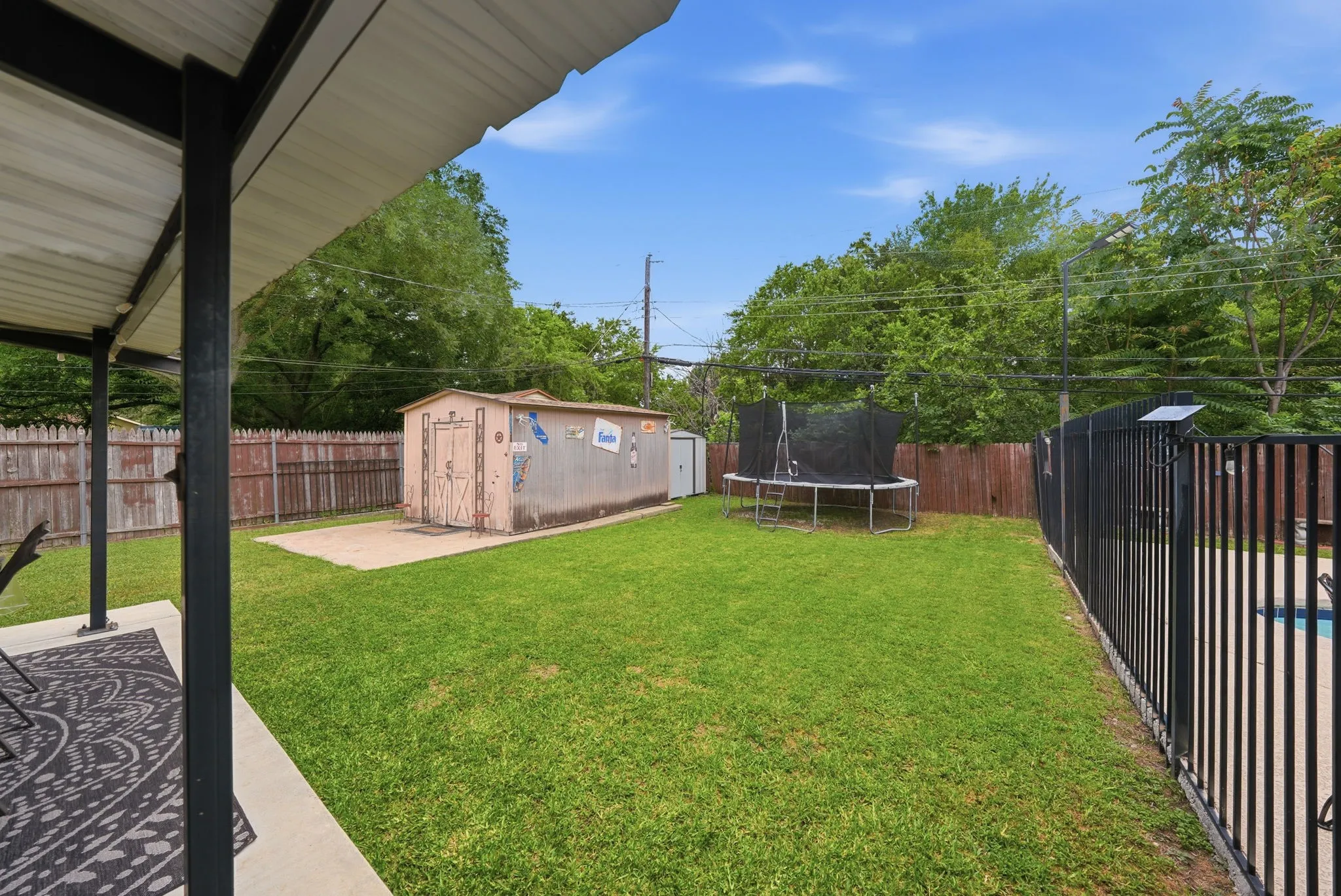 Expansive green lawn featuring a detached storage shed on a concrete pad, a black metal fence, and a wooden privacy fence