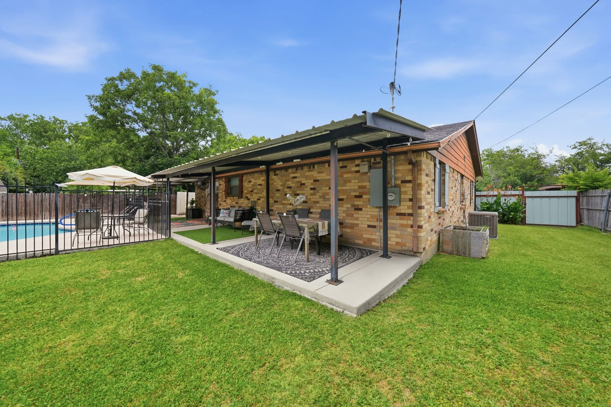 Expansive backyard featuring a covered patio, brick exterior, fenced swimming pool area, and a storage shed