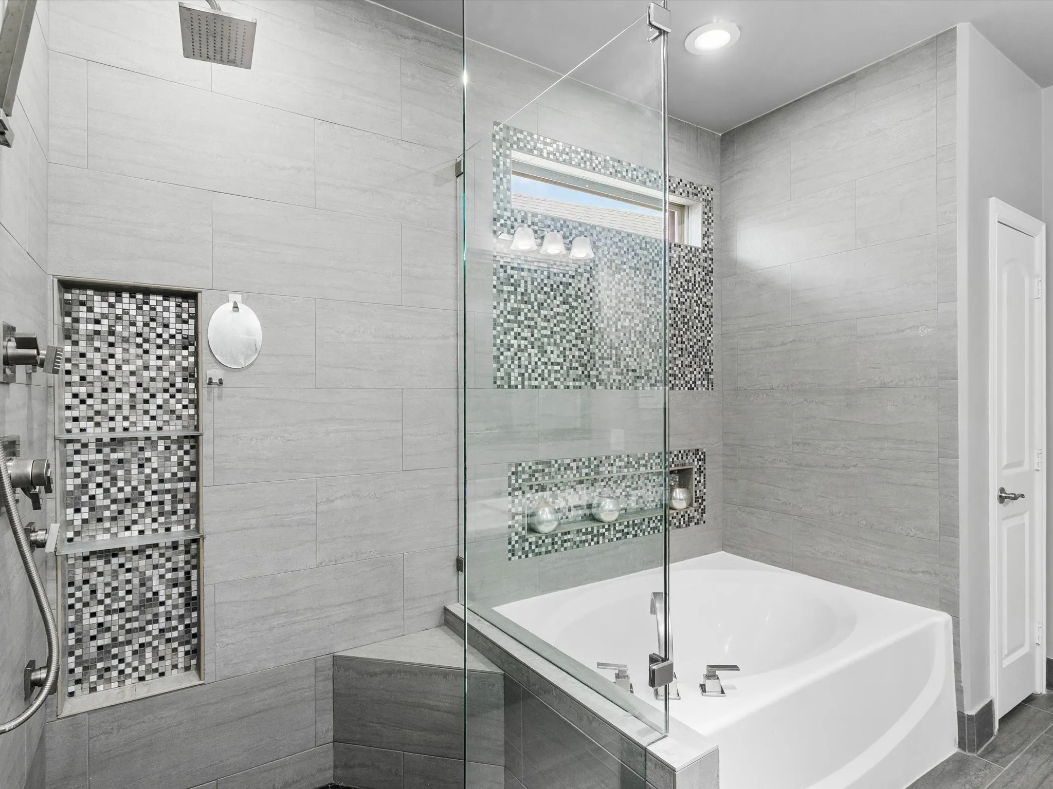 Walk-in shower with a rainfall showerhead, integrated tiled shelving, and a glass enclosure featuring an adjacent built-in soaking tub