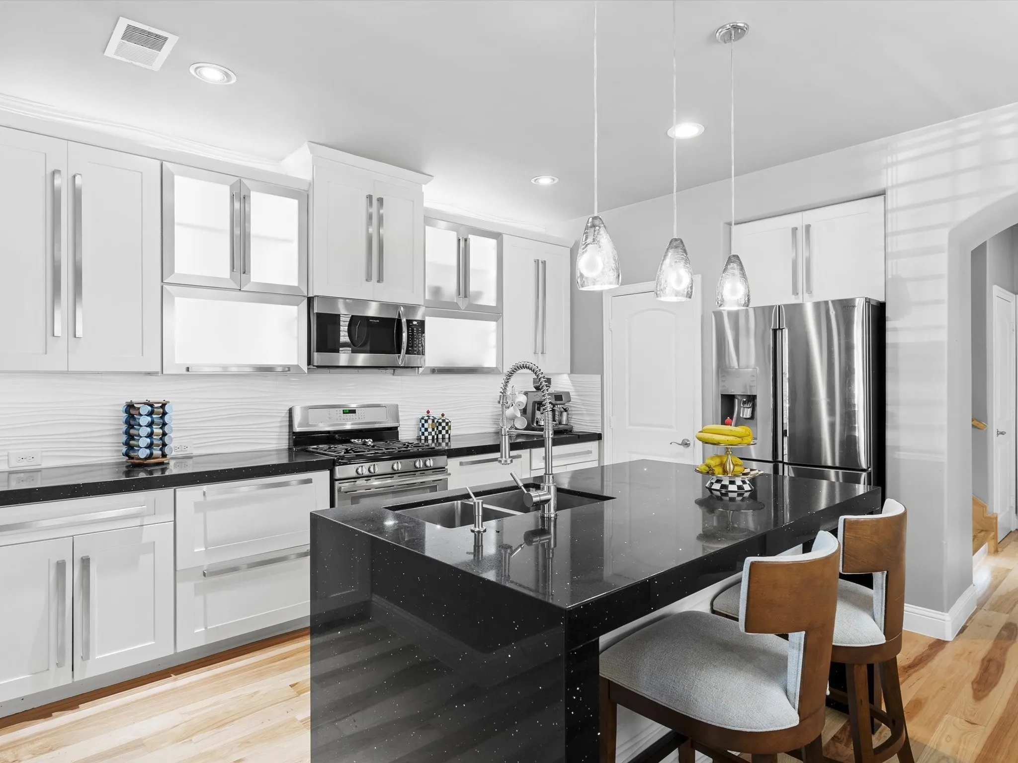 Modern kitchen featuring a large island with a double basin sink, black speckled countertops, and three pendant lights