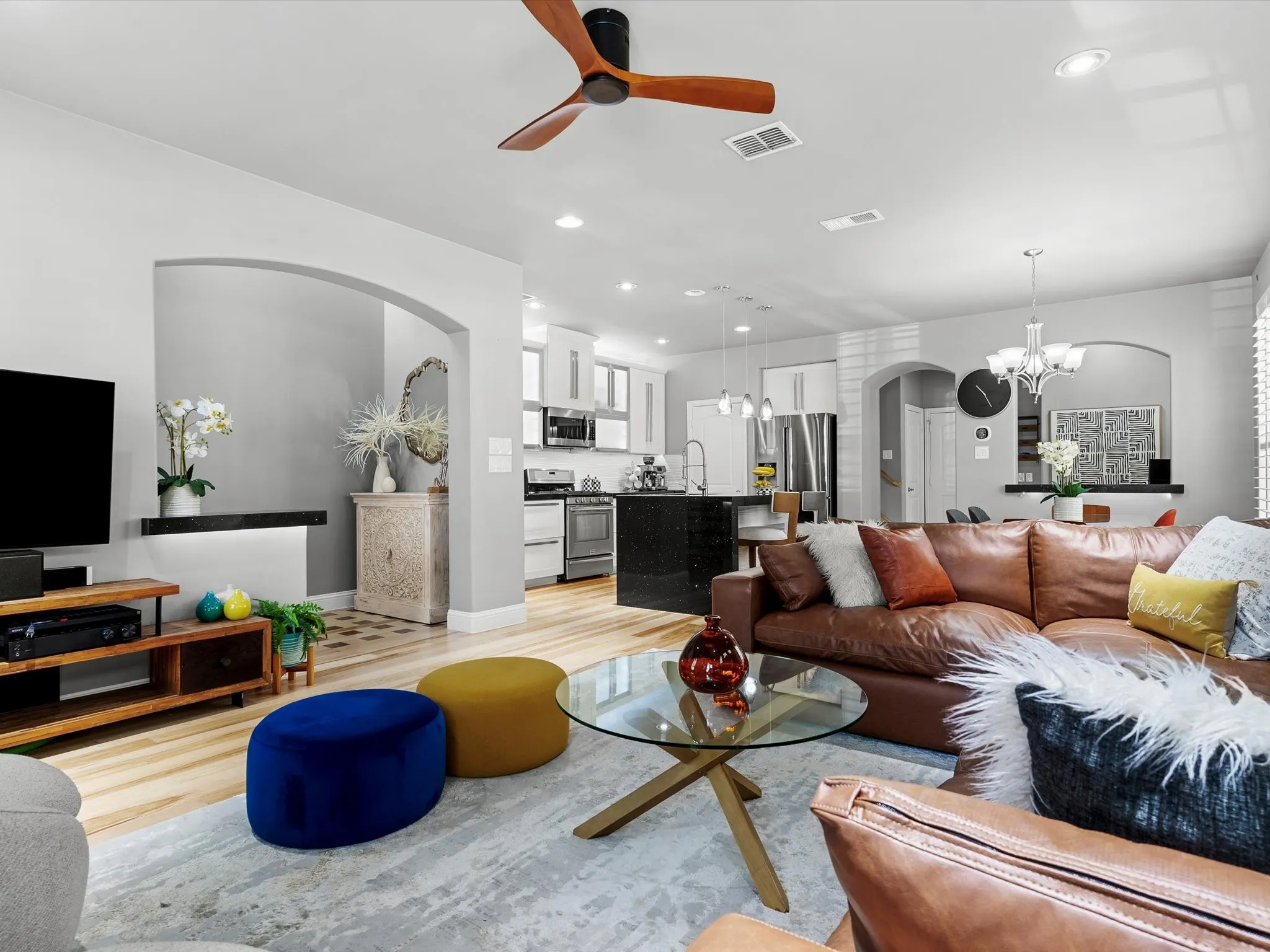 Open-concept living area featuring light wood-finish flooring, a modern ceiling fan, recessed lighting, and an arched entryway