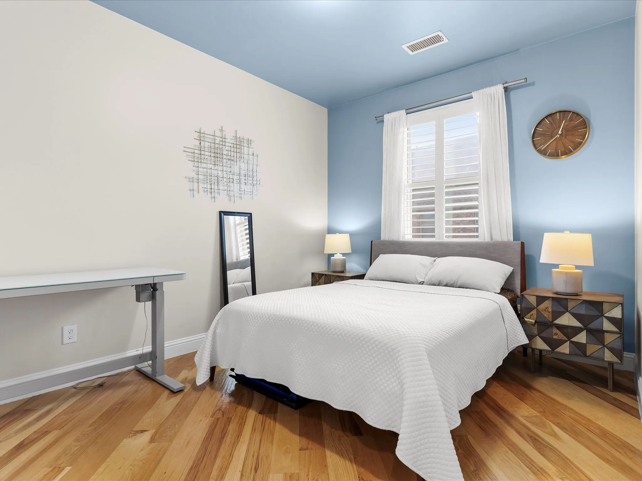 Bedroom featuring wood-finish flooring, a window with white shutters, and dual-tone wall paint
